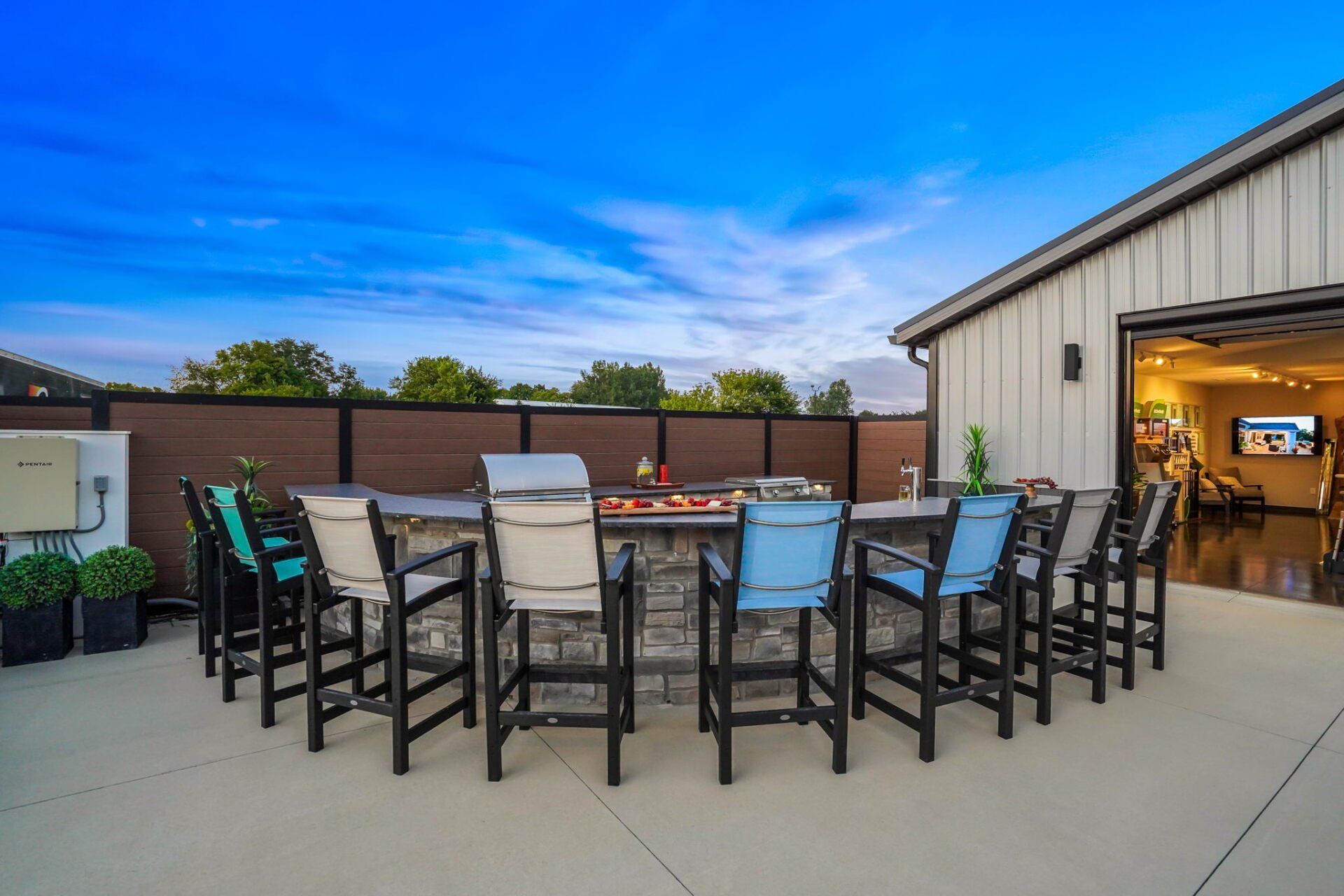Outdoor patio with chairs around a fire table beside an open garage, under a blue sky.