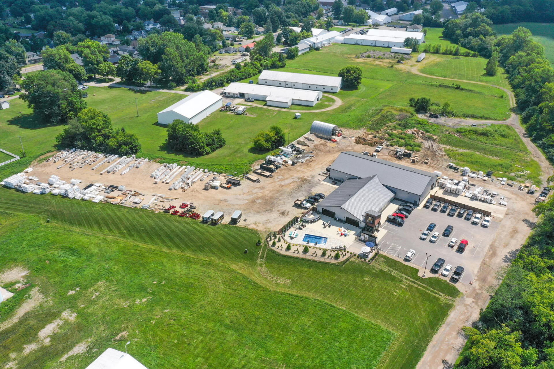 Aerial view of a rural farm with fields, barns, parked vehicles, and a swimming pool.