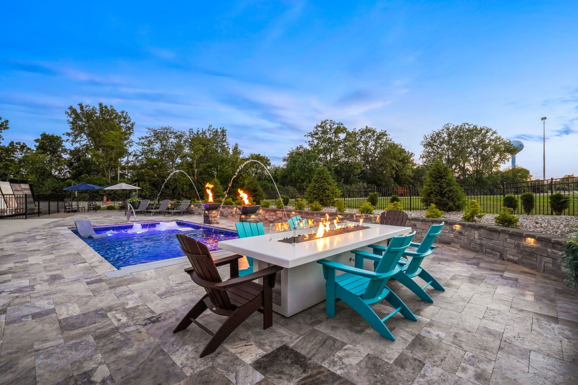 Outdoor patio with a lit fire table, turquoise chairs, and a blue pool at dusk