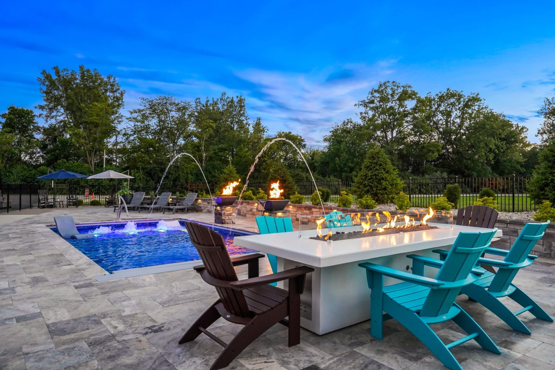 Backyard patio with pool, fire pit dining table, and turquoise chairs at sunset