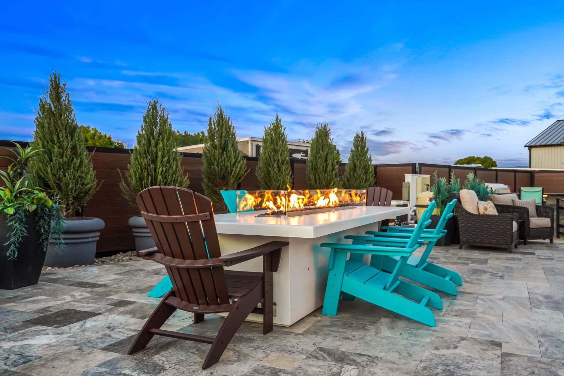 Outdoor patio with a fire pit table and colorful Adirondack chairs under a blue sky
