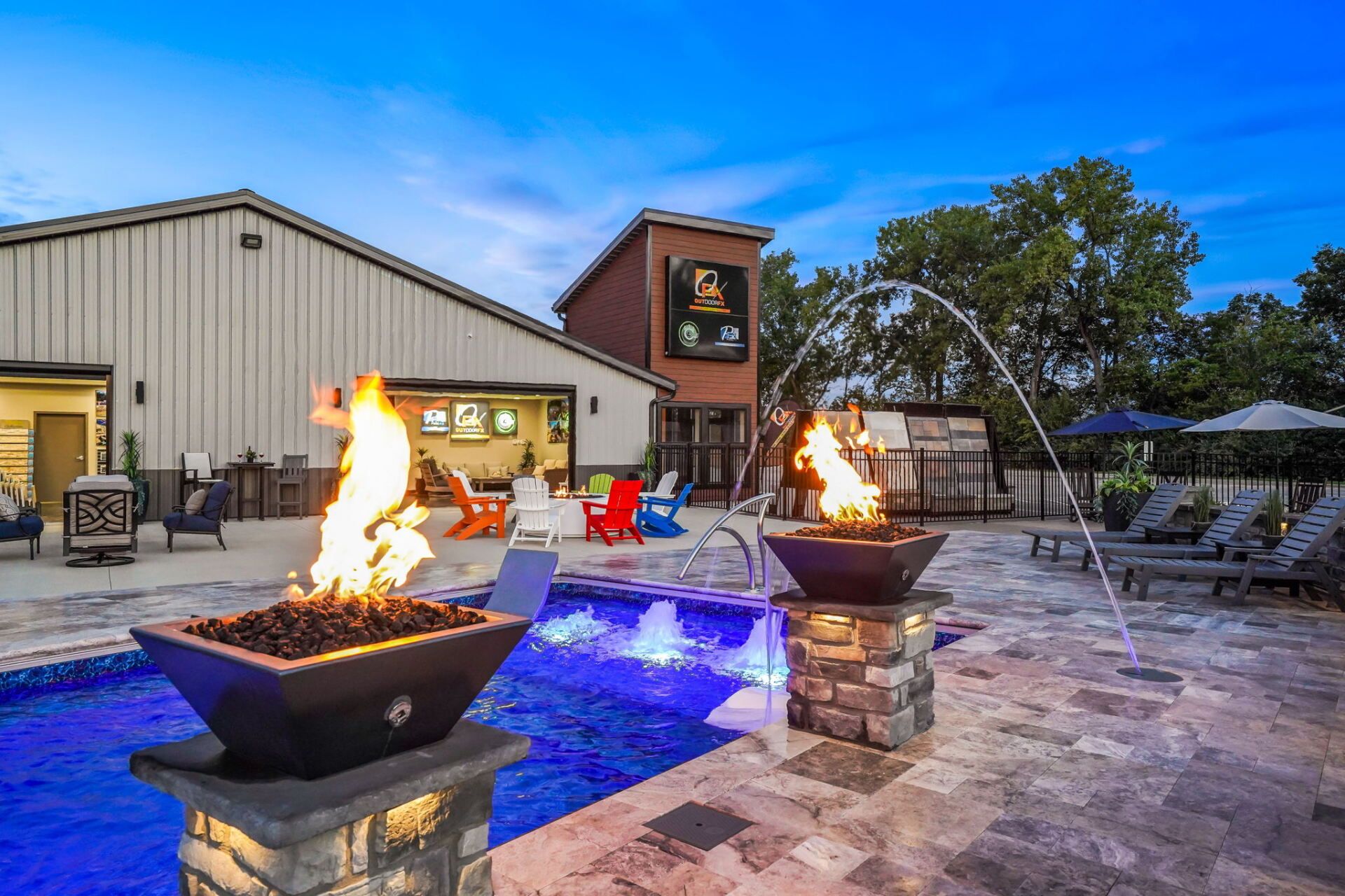 Outdoor patio with a blue-lit pool, fire bowls, and a building in the background