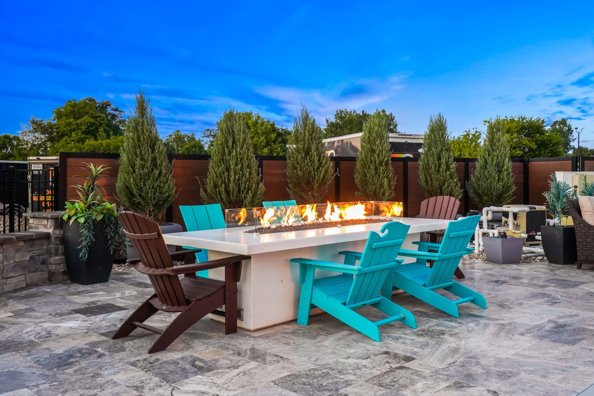 Outdoor patio with a long fire table, turquoise and brown chairs, and a stone seating area around a fire pit.