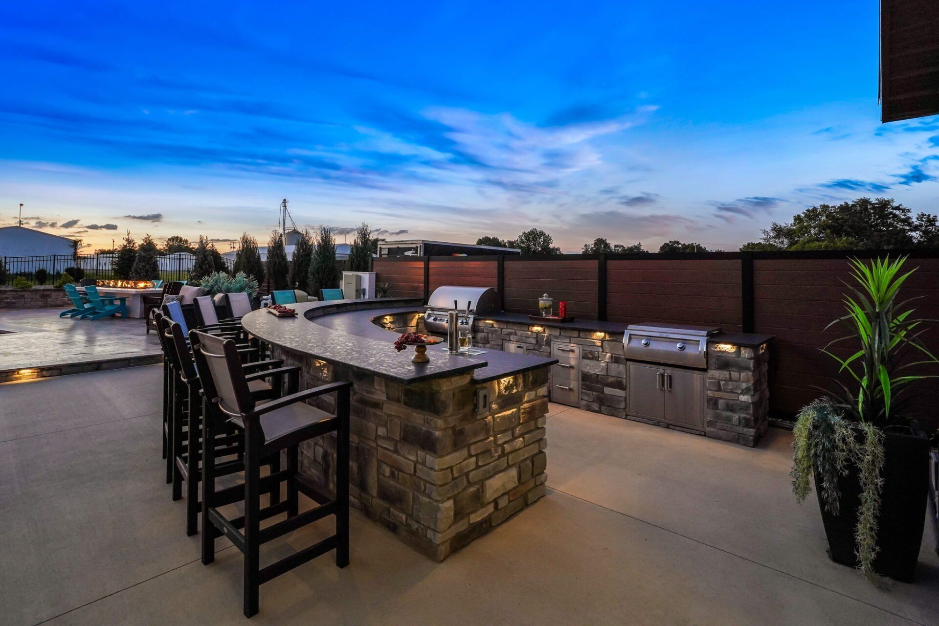 Rooftop patio with stone bar, barstools, grill, and city skyline at sunset
