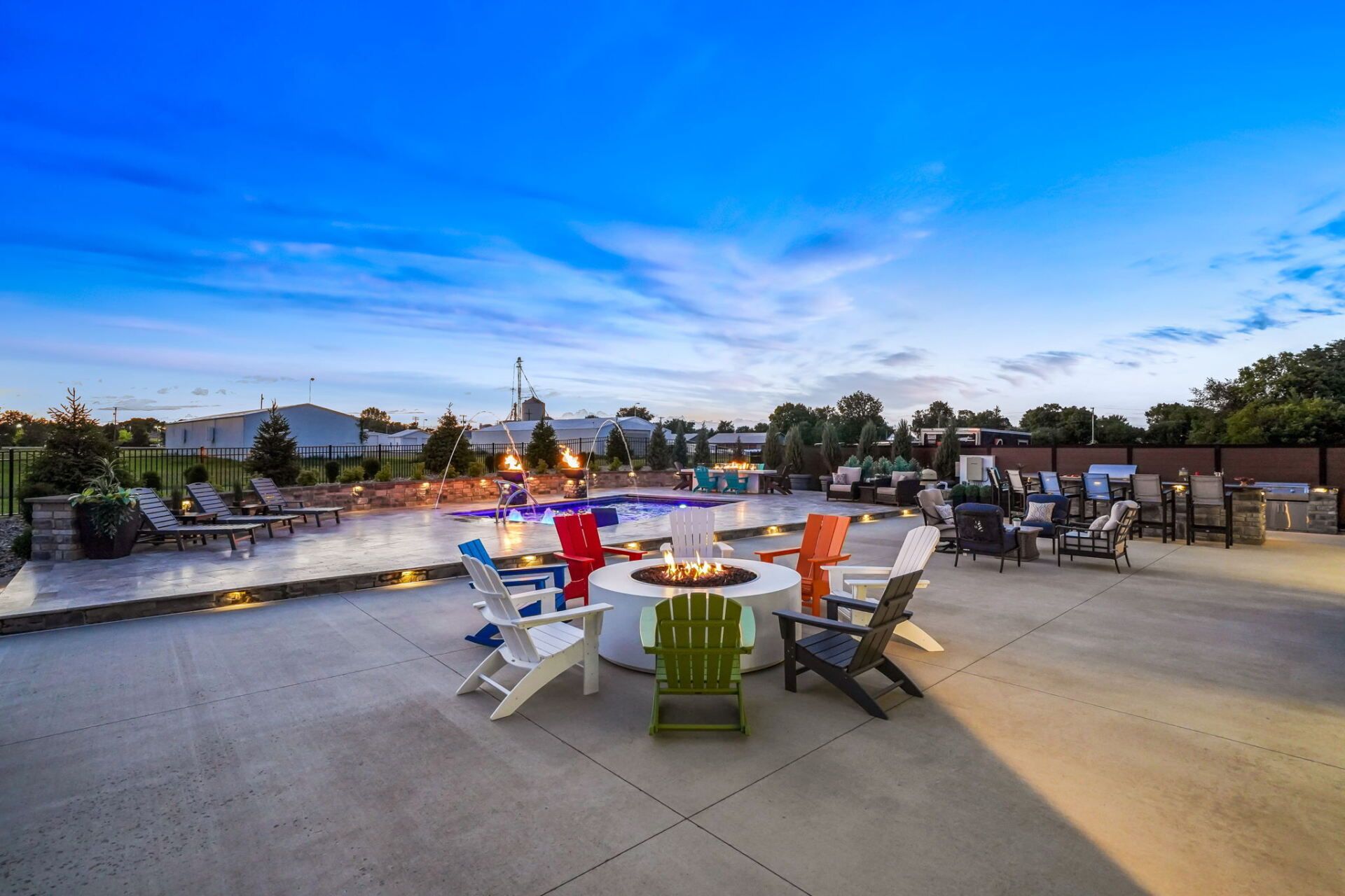 Outdoor patio with colorful chairs around a fire pit overlooking a landscaped area at dusk