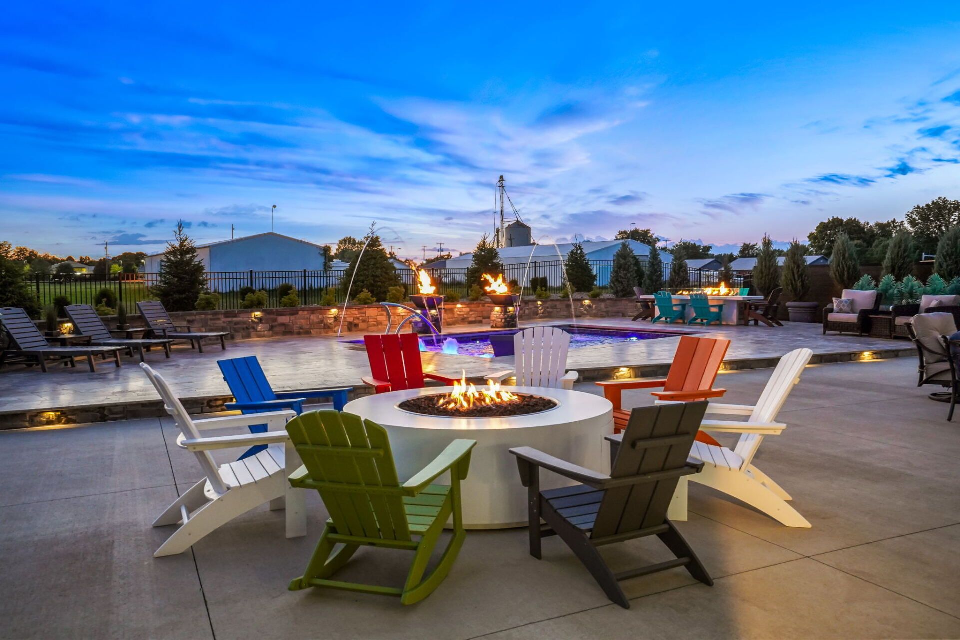 Colorful Adirondack chairs around a fire pit on a rooftop patio at dusk