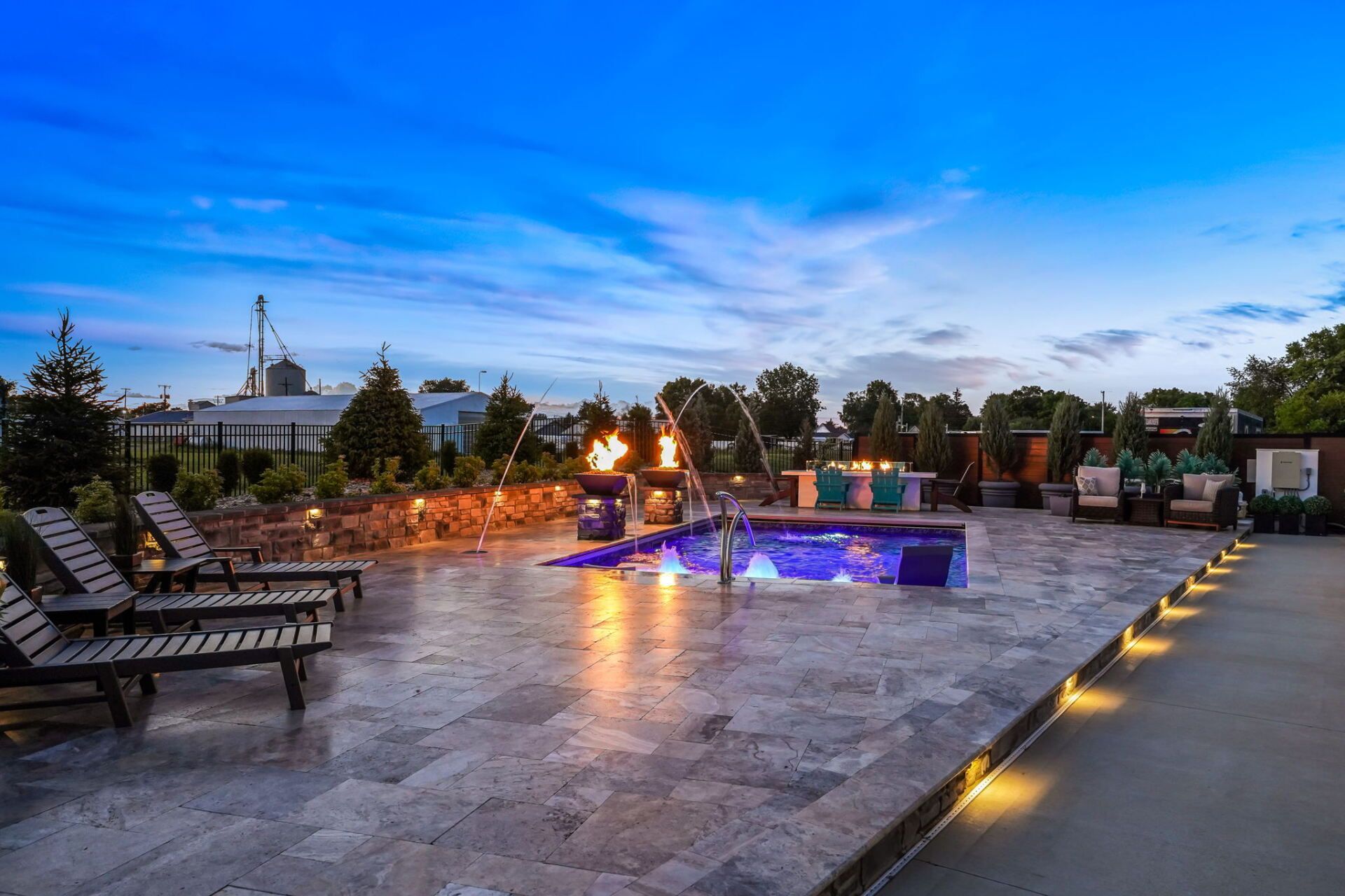 Outdoor patio with lit fountain, lounge chairs, and sunset sky