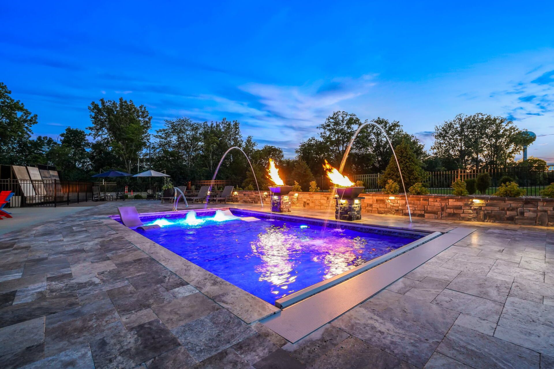 Lit blue pool with fire features on a stone patio at dusk