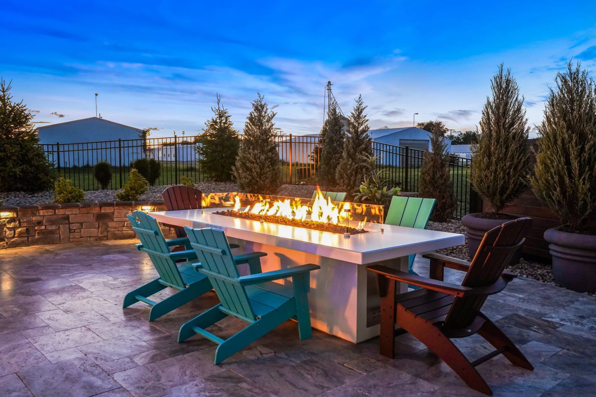 Outdoor patio with a lit fire table, teal lounge chairs, and trees at dusk