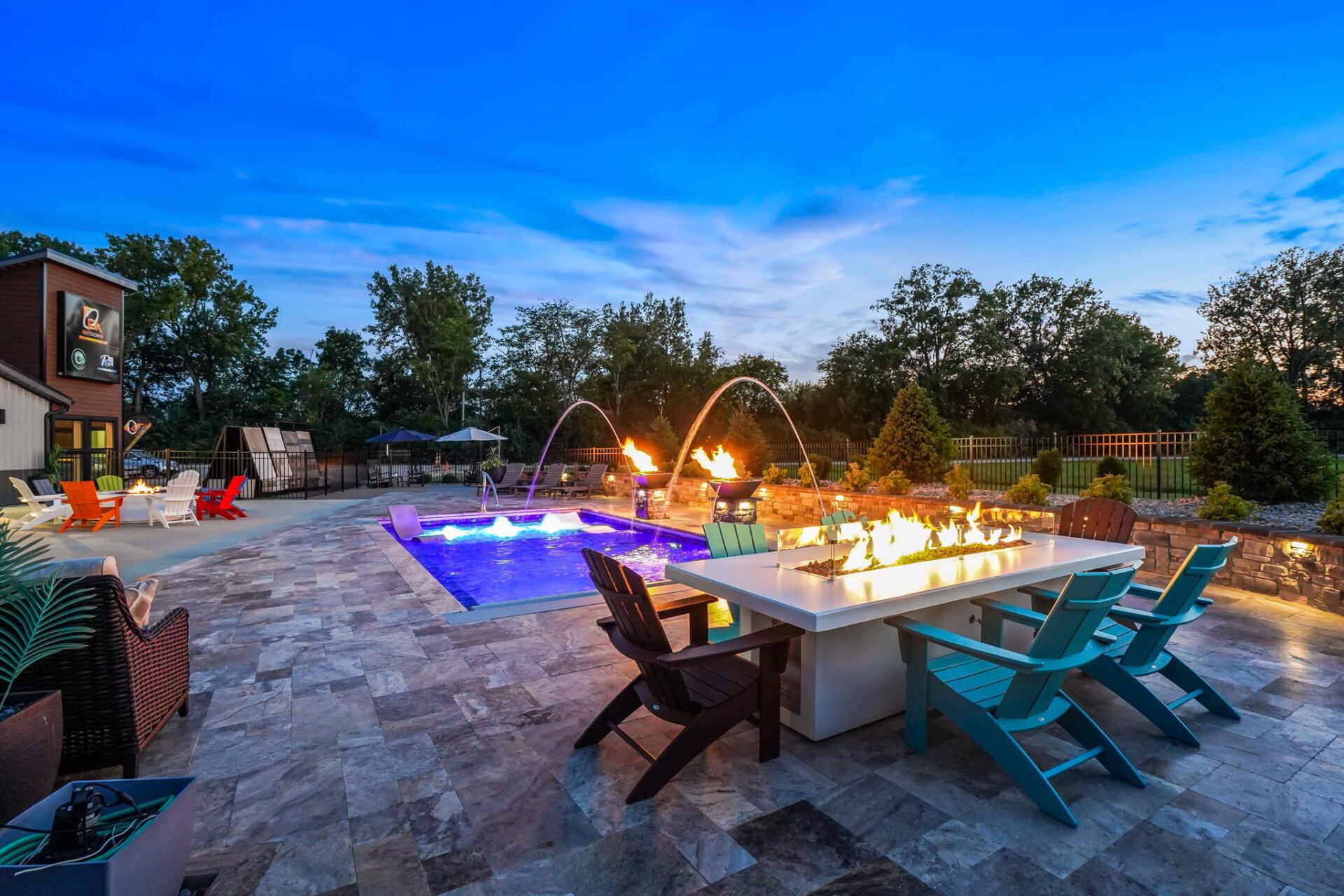 Poolside patio at dusk with lit dining table, turquoise chairs, and glowing fire features