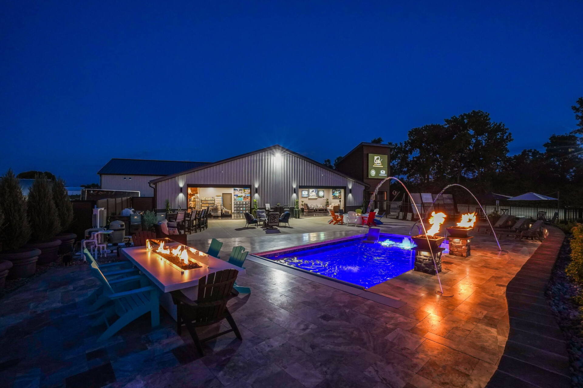 Nighttime resort patio with lit pool, fire pit, and lounge seating beside a modern building