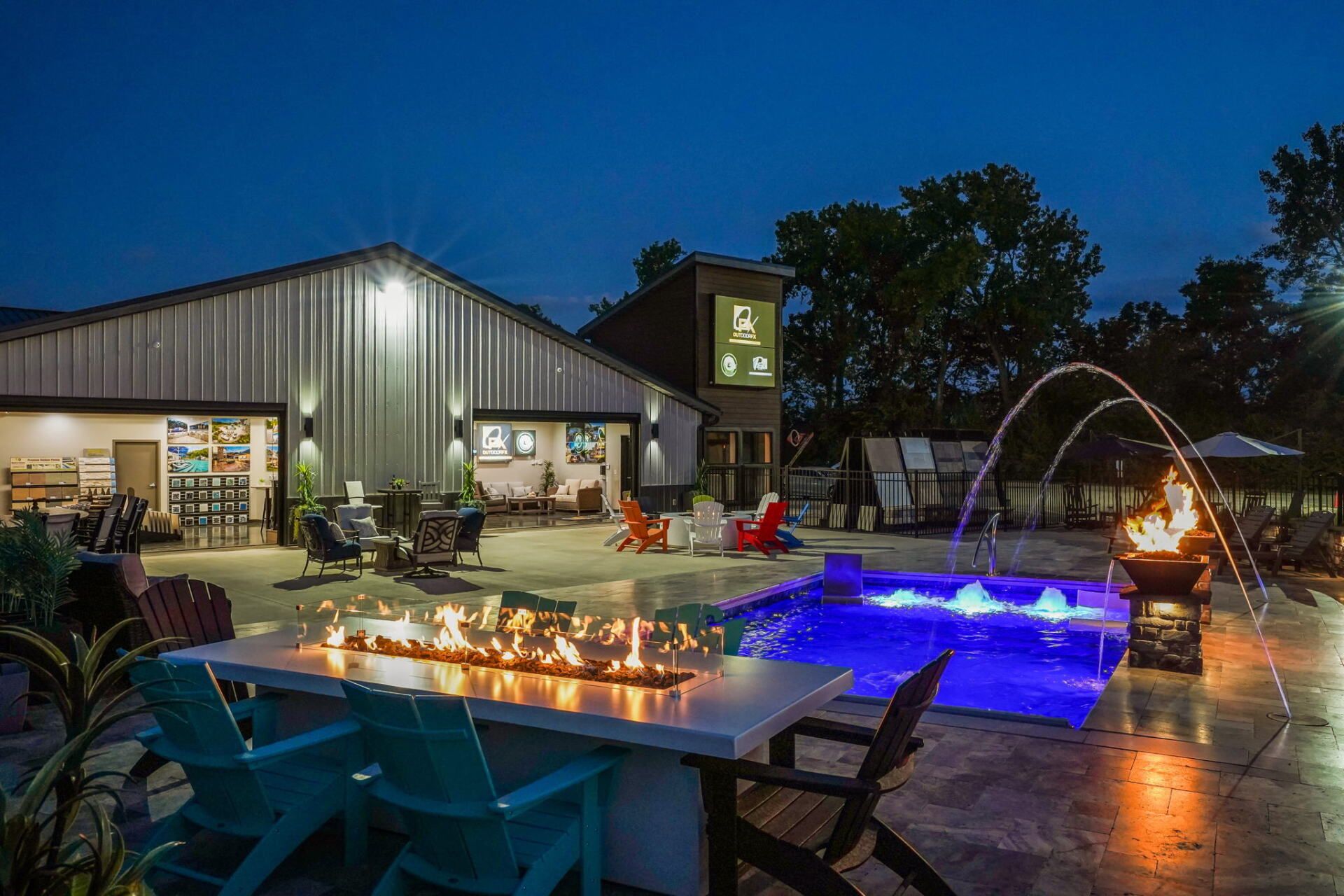 Backyard patio with lit pool, fire pit, and string lights beside a modern house at dusk