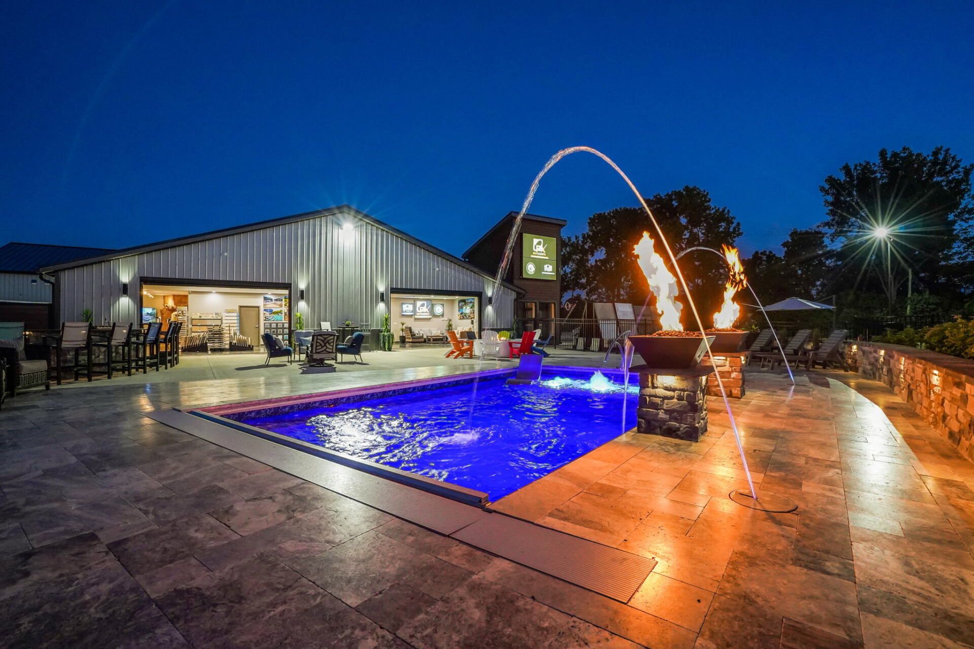 Modern house with lit backyard pool at night, arched water feature, and stone patio