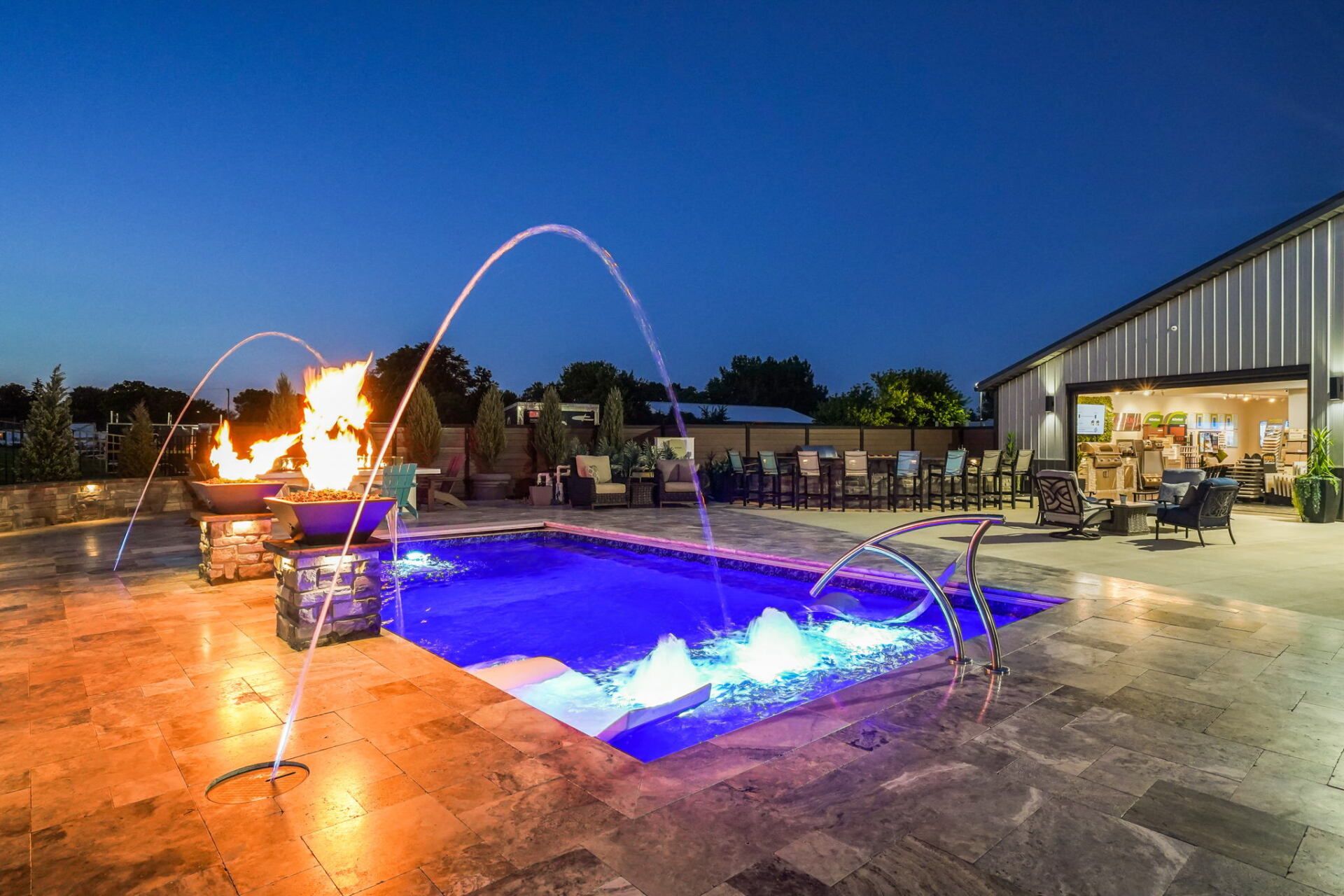 Nighttime patio with a lit fountain pool and fire feature beside a modern building