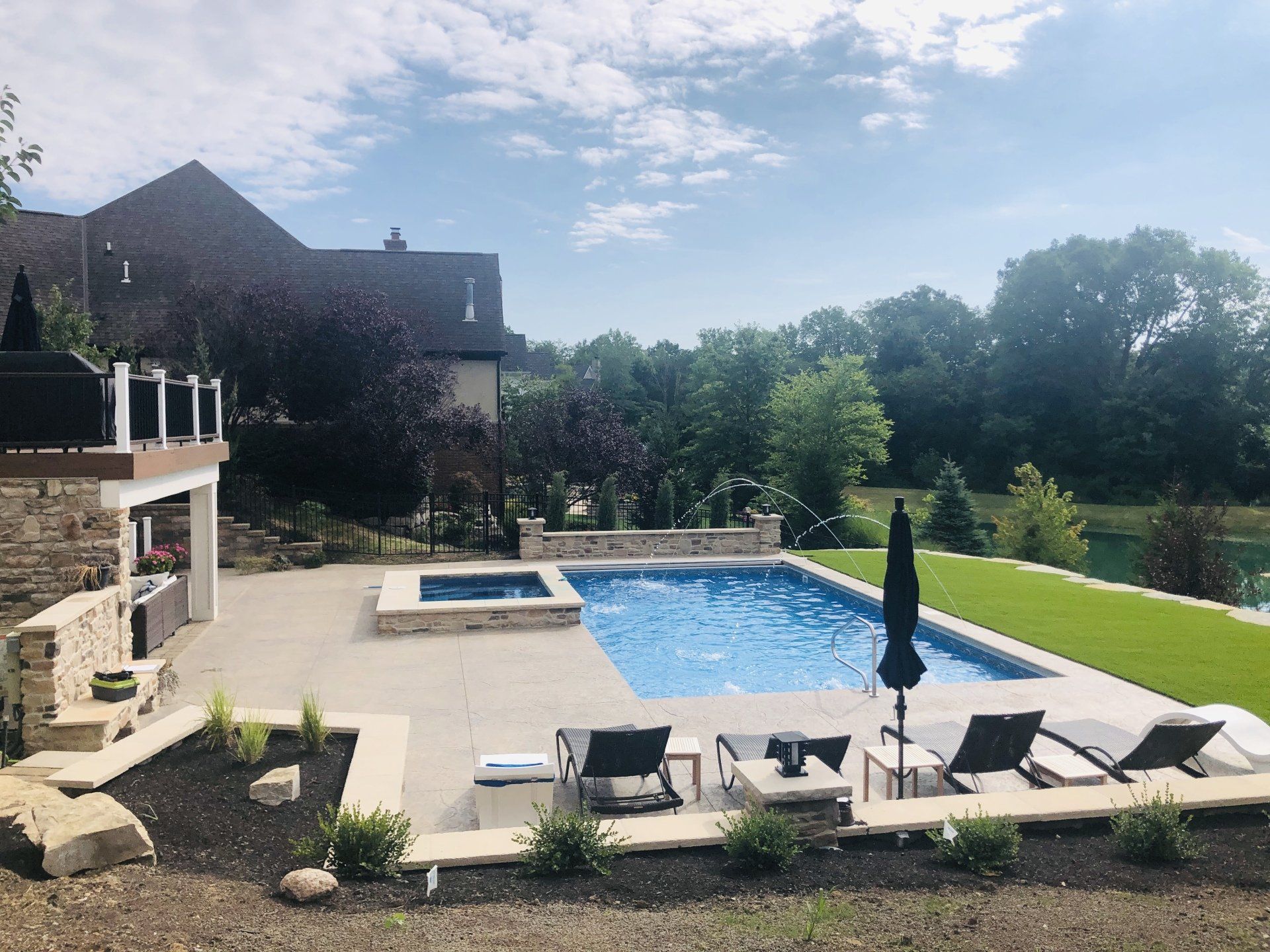 Backyard pool with lounge chairs, patio, and a house under a sunny sky