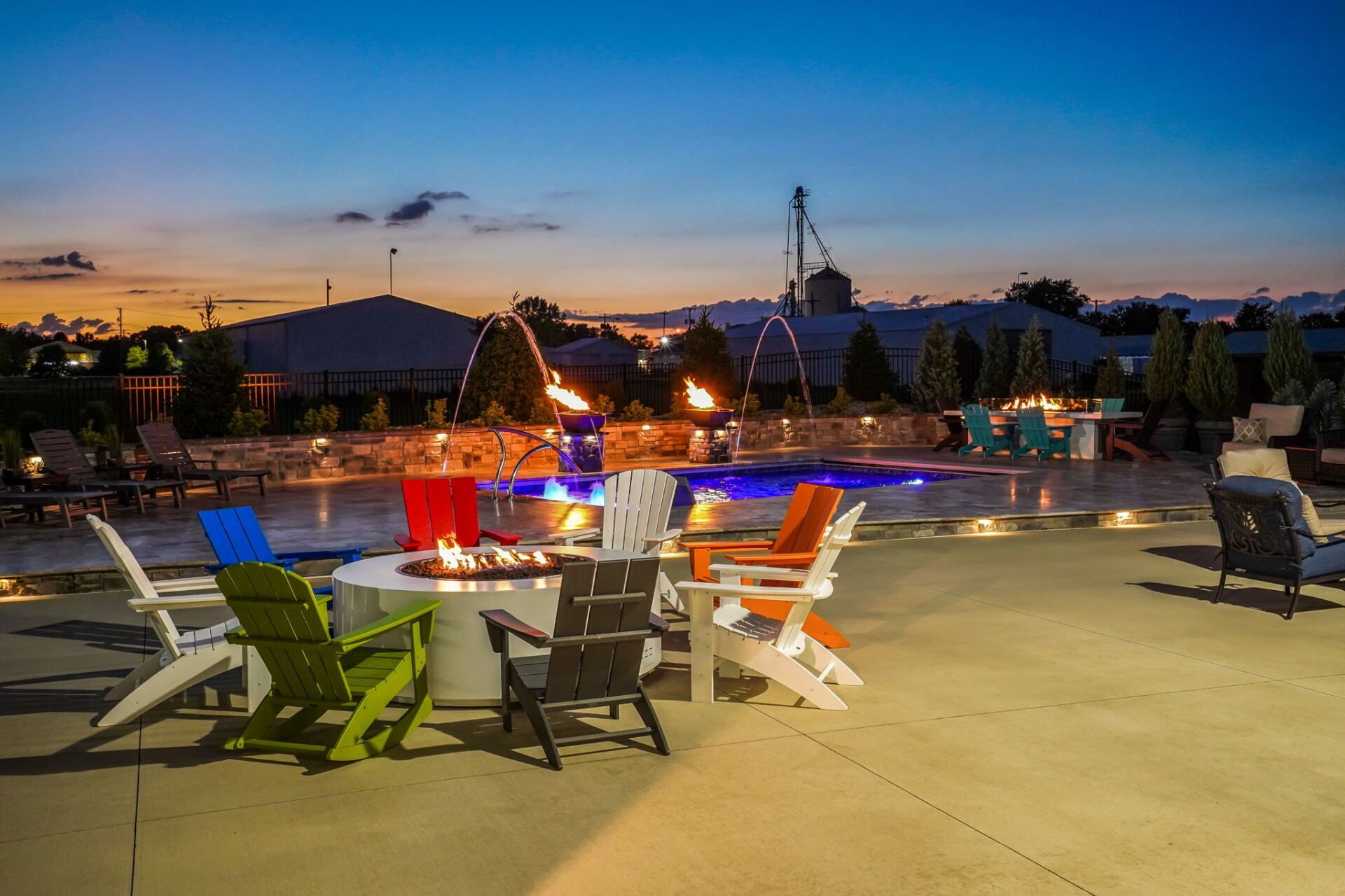 Outdoor patio with colorful chairs, lit tables, and a pool at dusk under a twilight sky