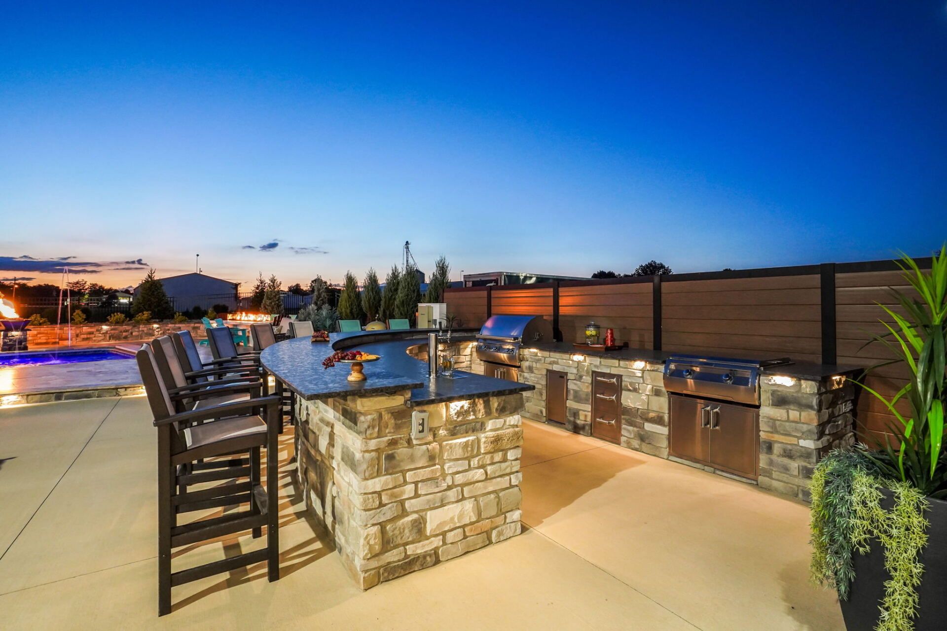 Outdoor patio with bar seating, stone counters, and warm lighting at sunset.
