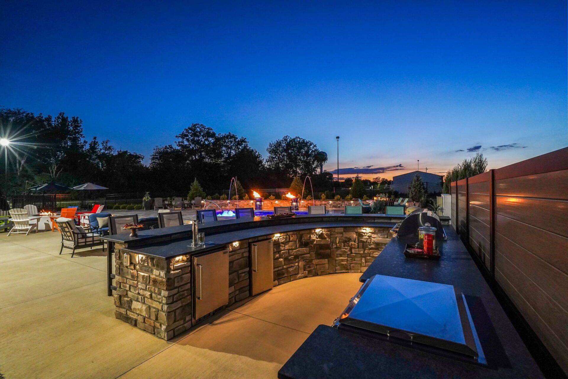 Outdoor stone bar and patio at dusk with blue sky, warm lights, and people seated around tables