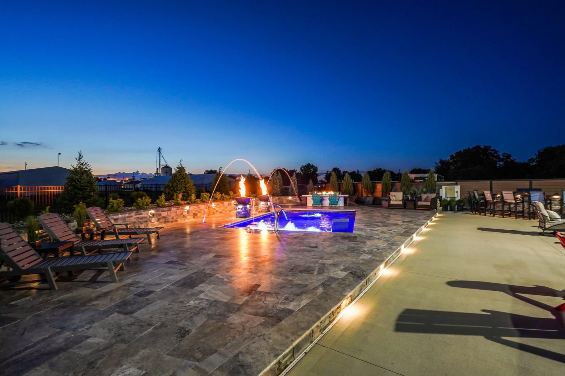 Outdoor rooftop terrace at dusk with lit lounge area, pool, and rows of chairs under a dark blue sky