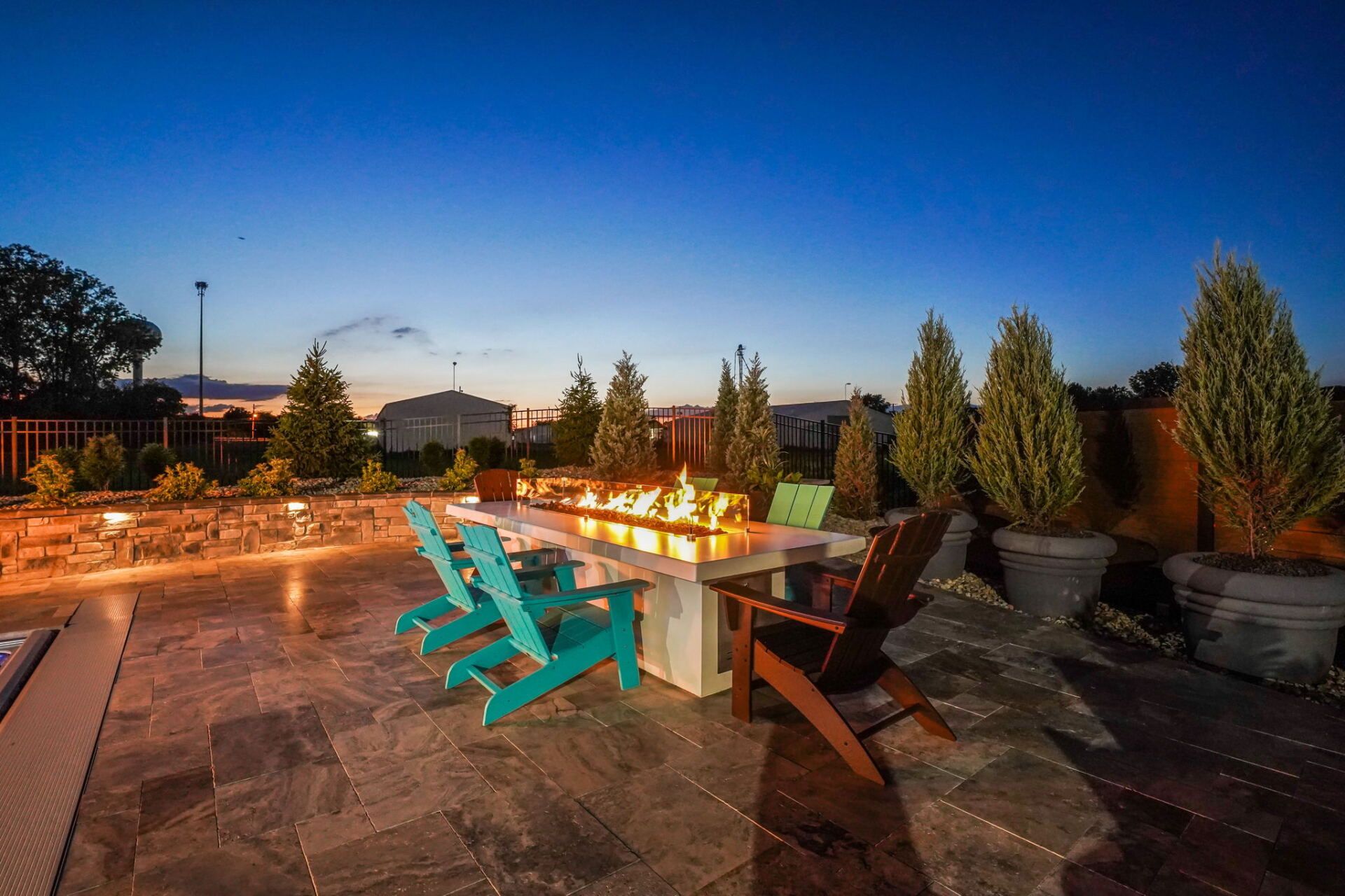 Outdoor patio at dusk with turquoise lounge chairs, tables, and potted plants under a blue sky.
