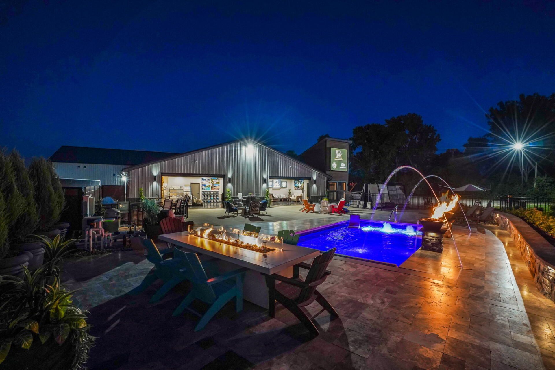 Backyard patio at night with lit swimming pool, lounge chairs, and a modern house in the background