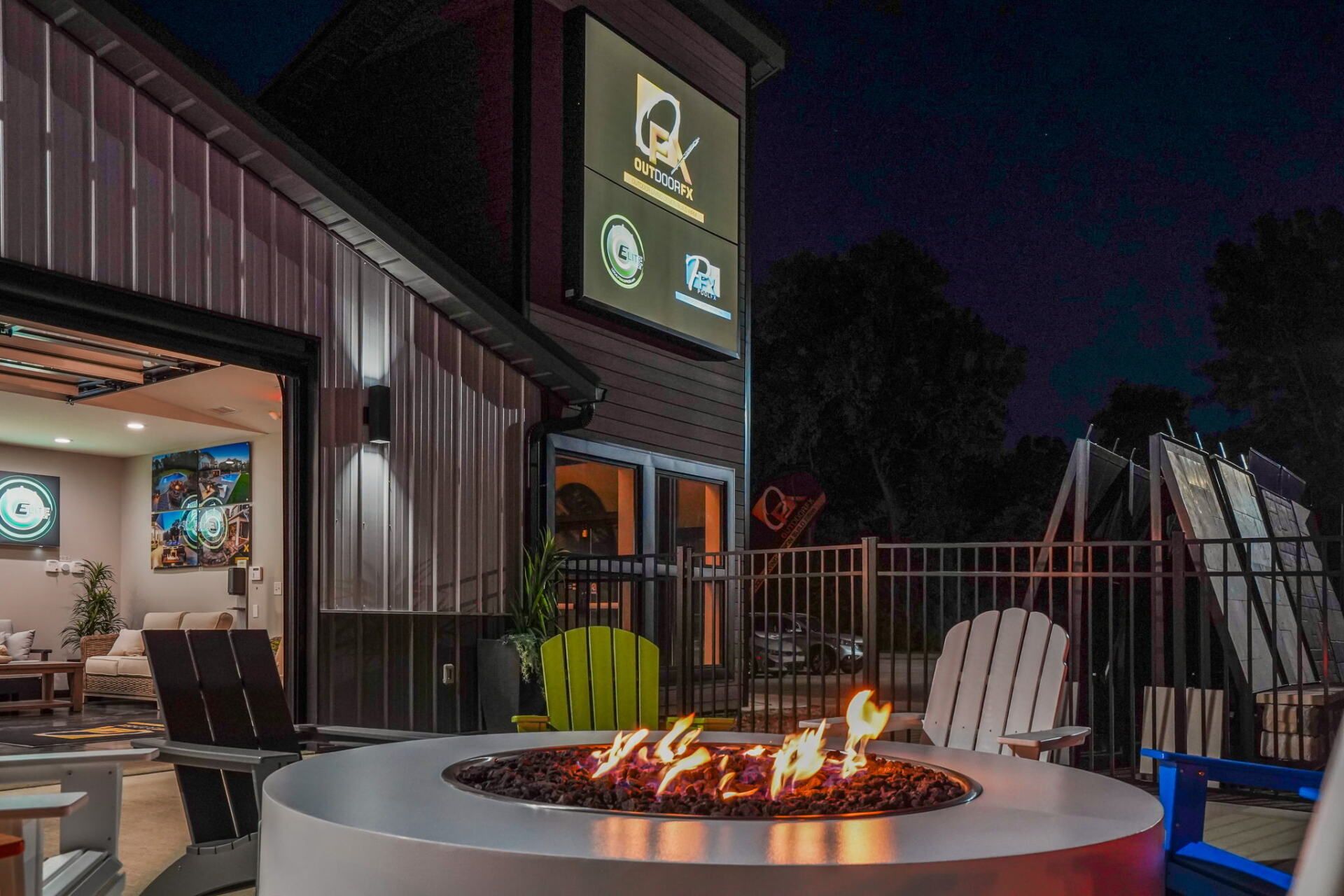 Outdoor patio with a fire pit, lounge chairs, and a lit building at dusk