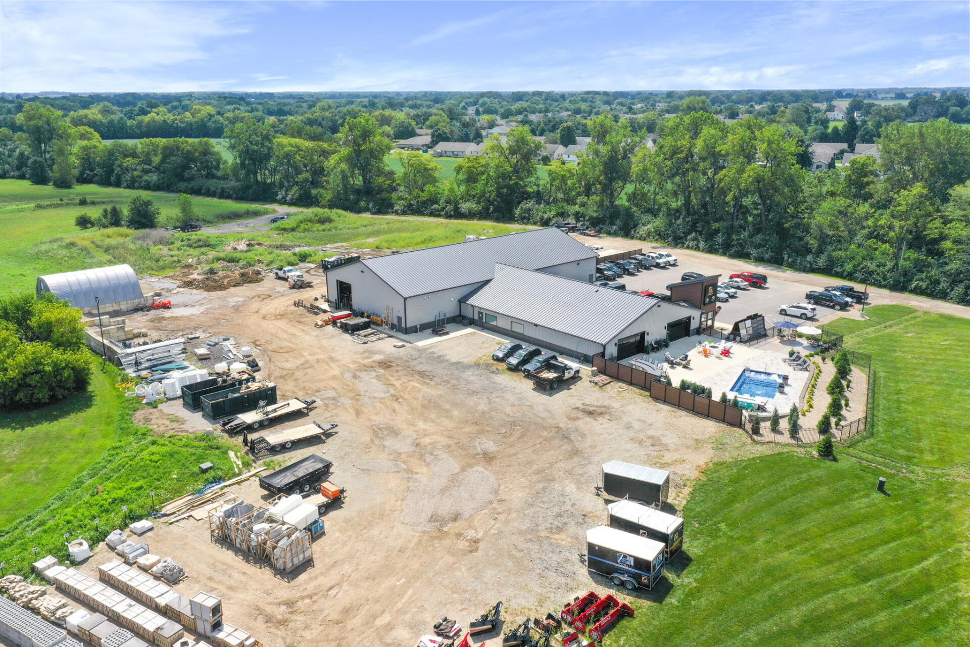 Aerial view of a rural construction site with buildings, equipment, and parked trucks amid green fields