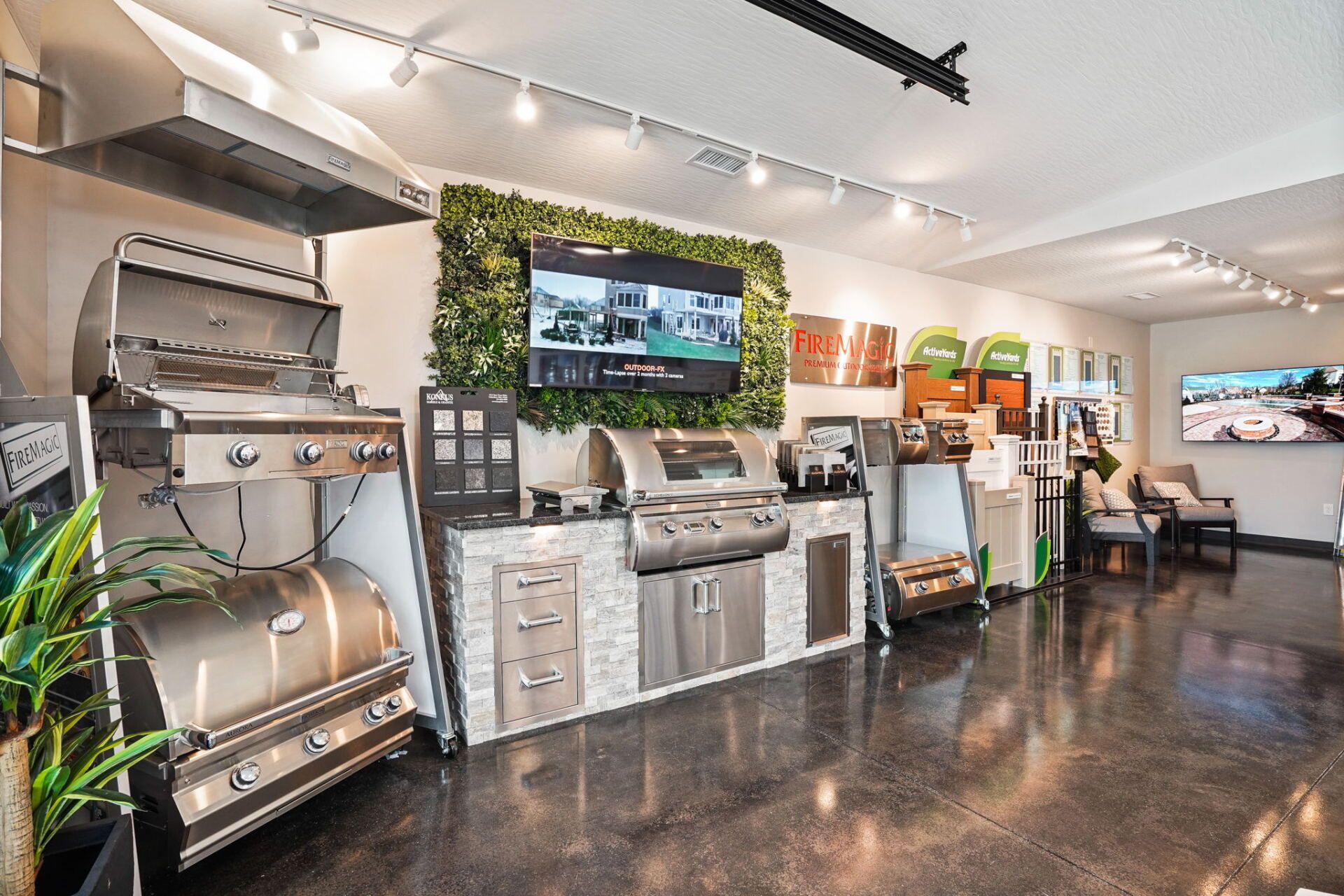 Modern outdoor kitchen showroom with stainless grills, TVs, and polished concrete floor