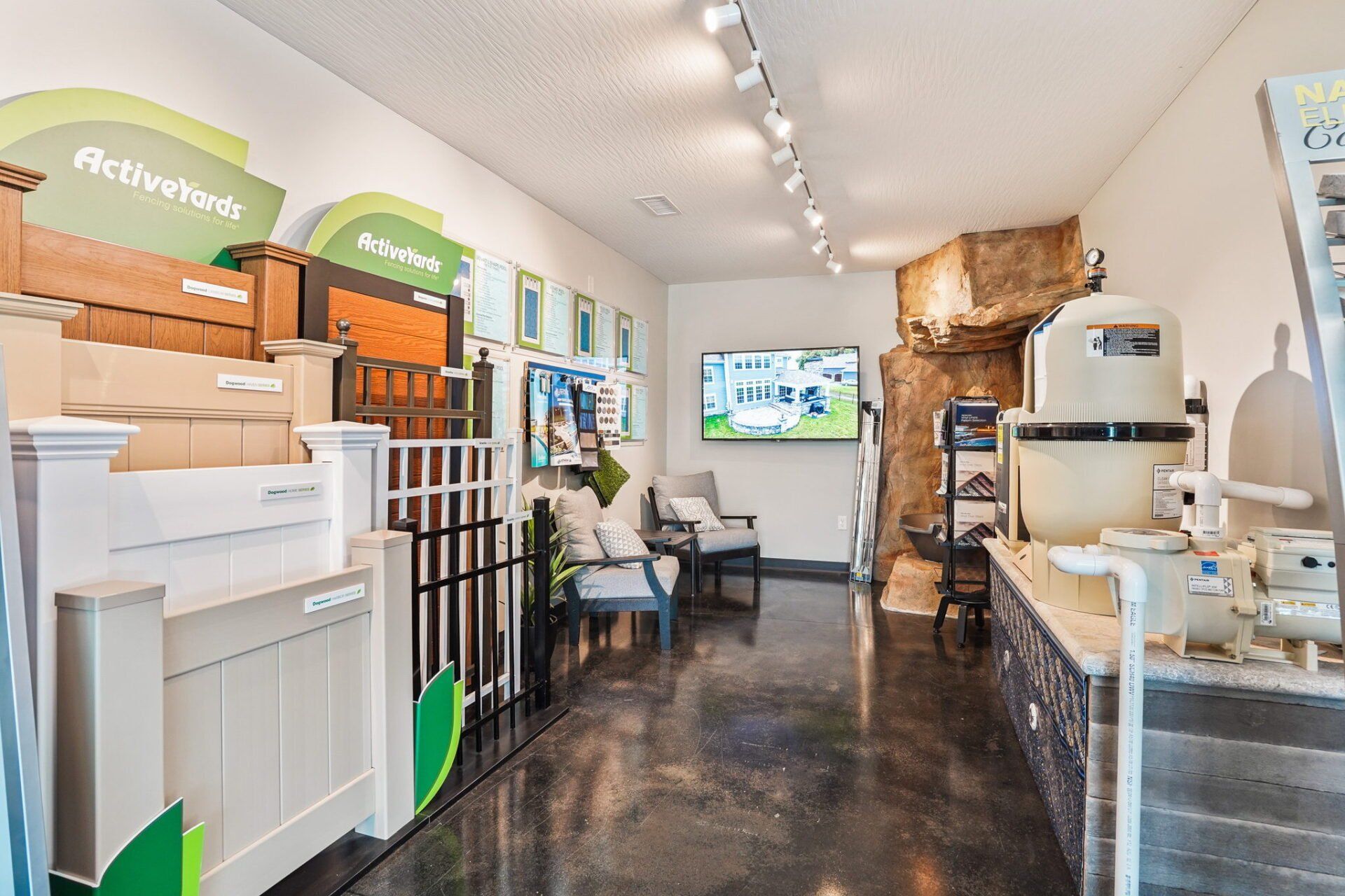 Bright showroom interior with flooring displays, samples, chairs, and a wall-mounted TV on a polished dark floor.