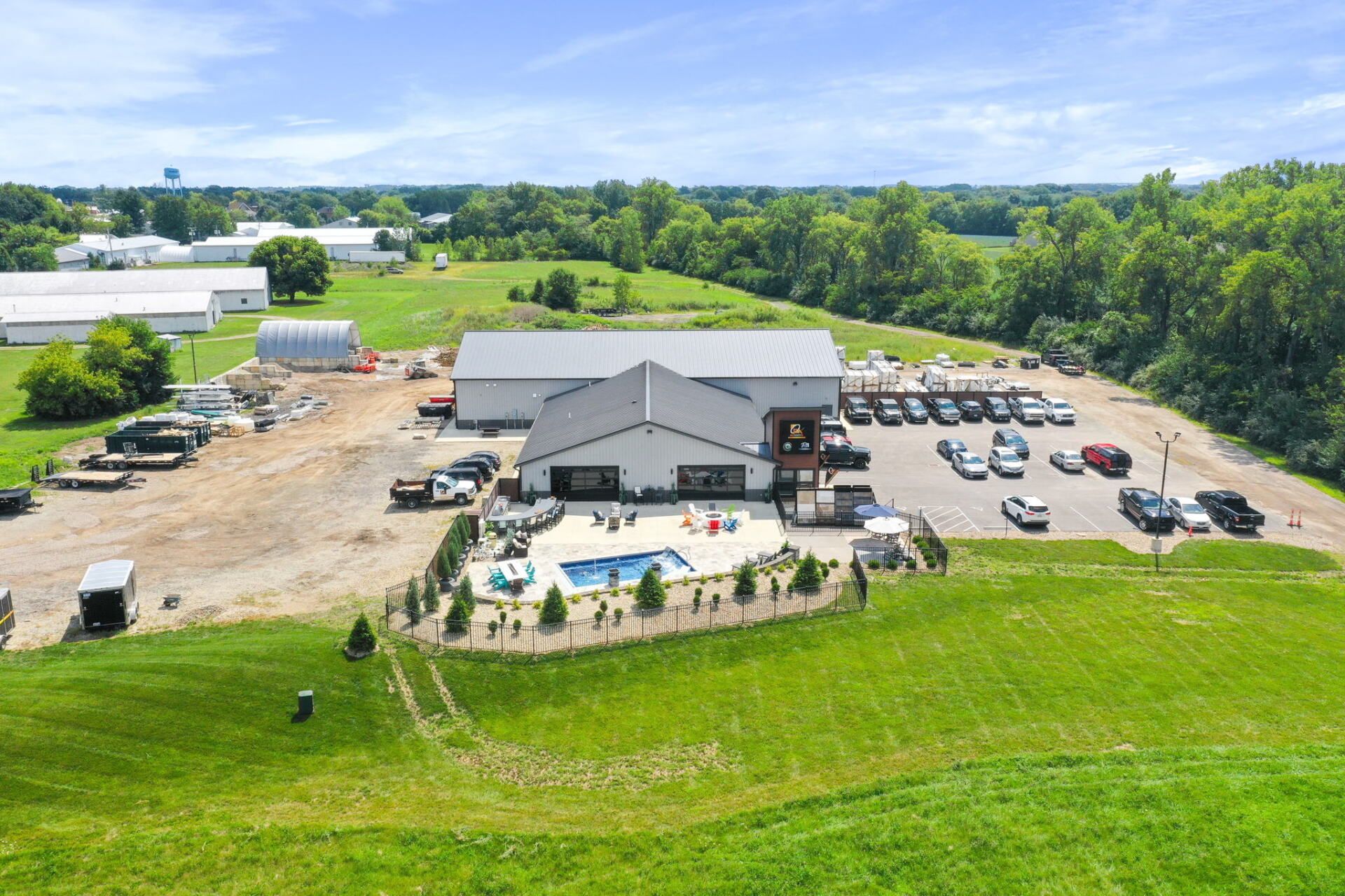 Aerial view of a white building, patio seating, parked cars, and green fields on a sunny day