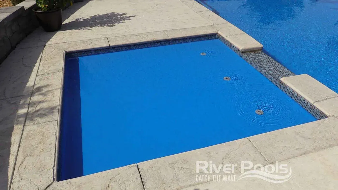 Empty blue swimming pool with a stone deck and steps beside it, viewed from above.