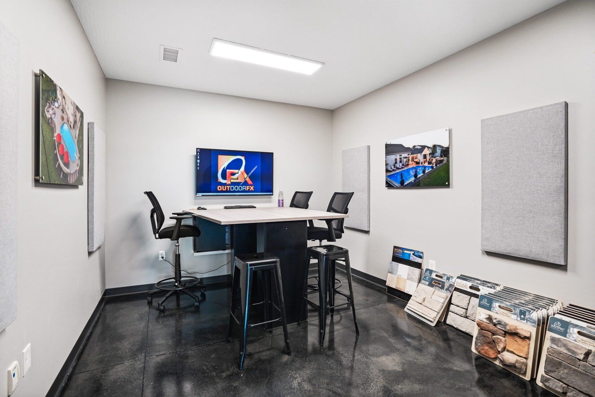 Small office meeting room with a TV display, table, chairs, wall art, and brochures lined along the wall.