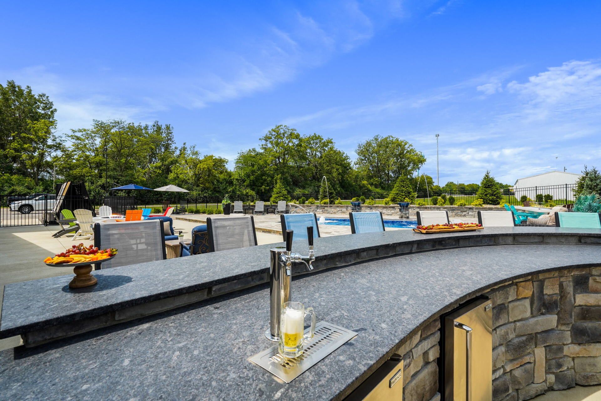 Outdoor pool deck with black stone wall, a drink on the ledge, and blue sky over trees and umbrellas