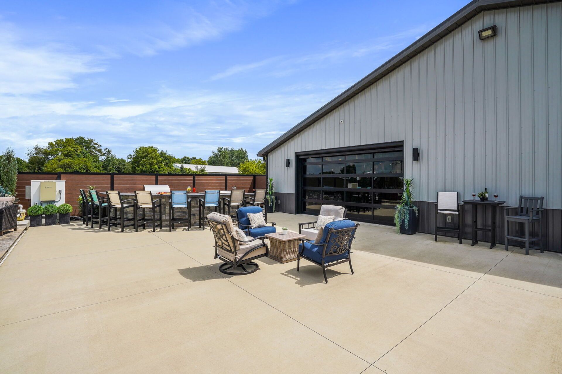 Outdoor patio with chairs and tables beside a white building and open garage door on a sunny day