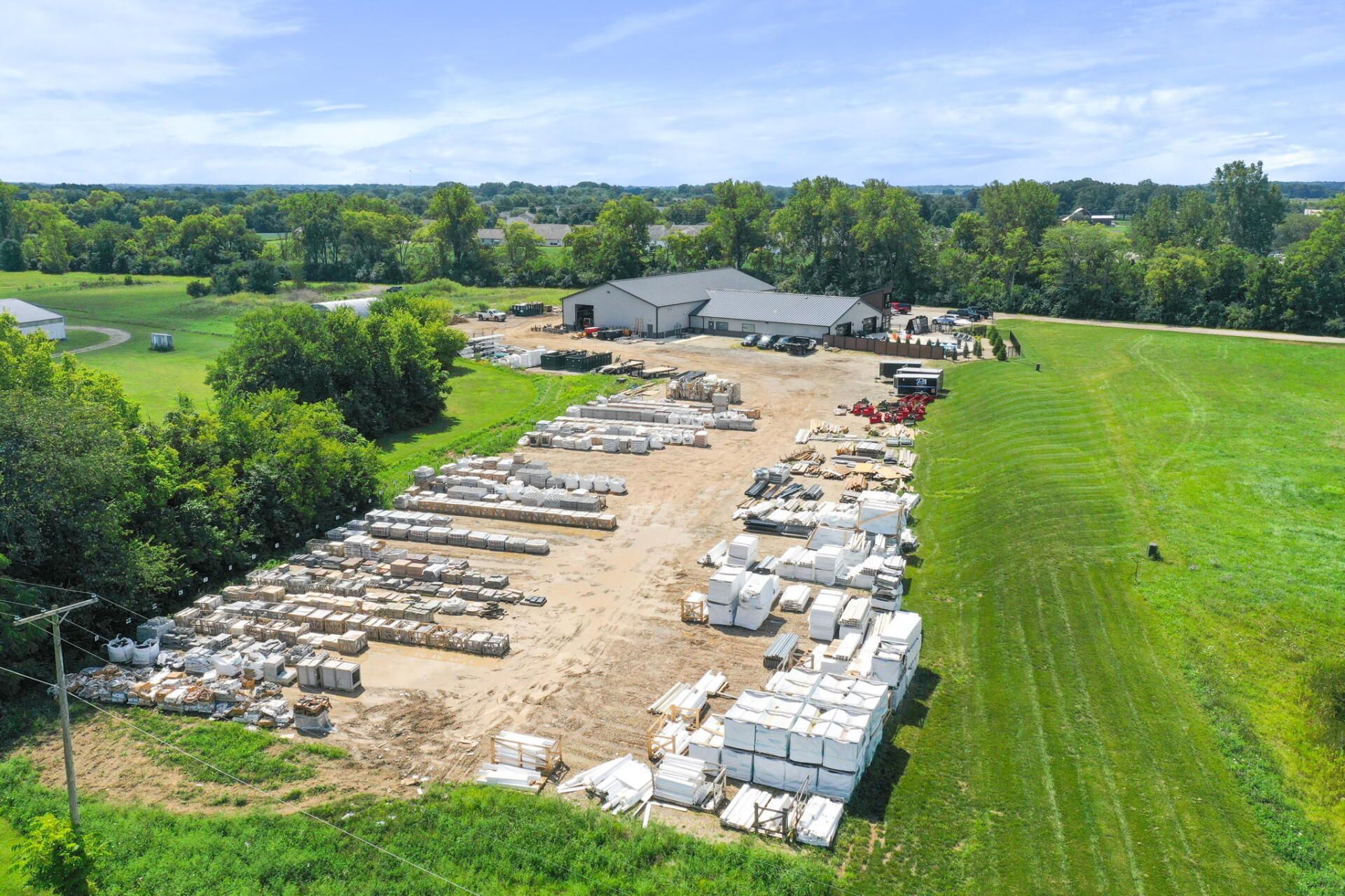 Aerial view of a lumber yard with stacks of boards and building materials beside green fields.