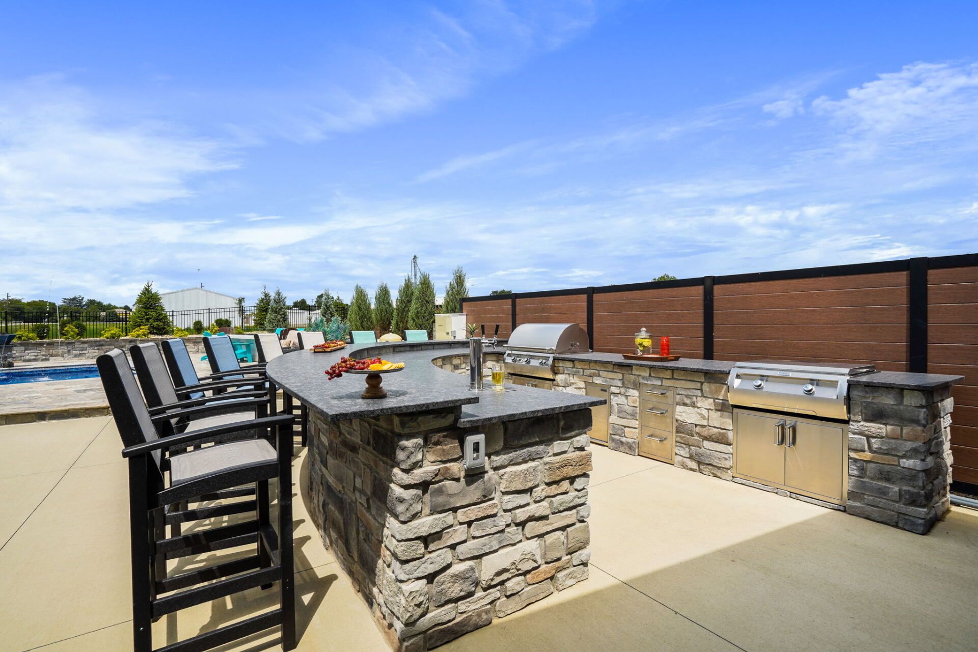 Outdoor patio with stone bar, high chairs, and grill under a bright blue sky