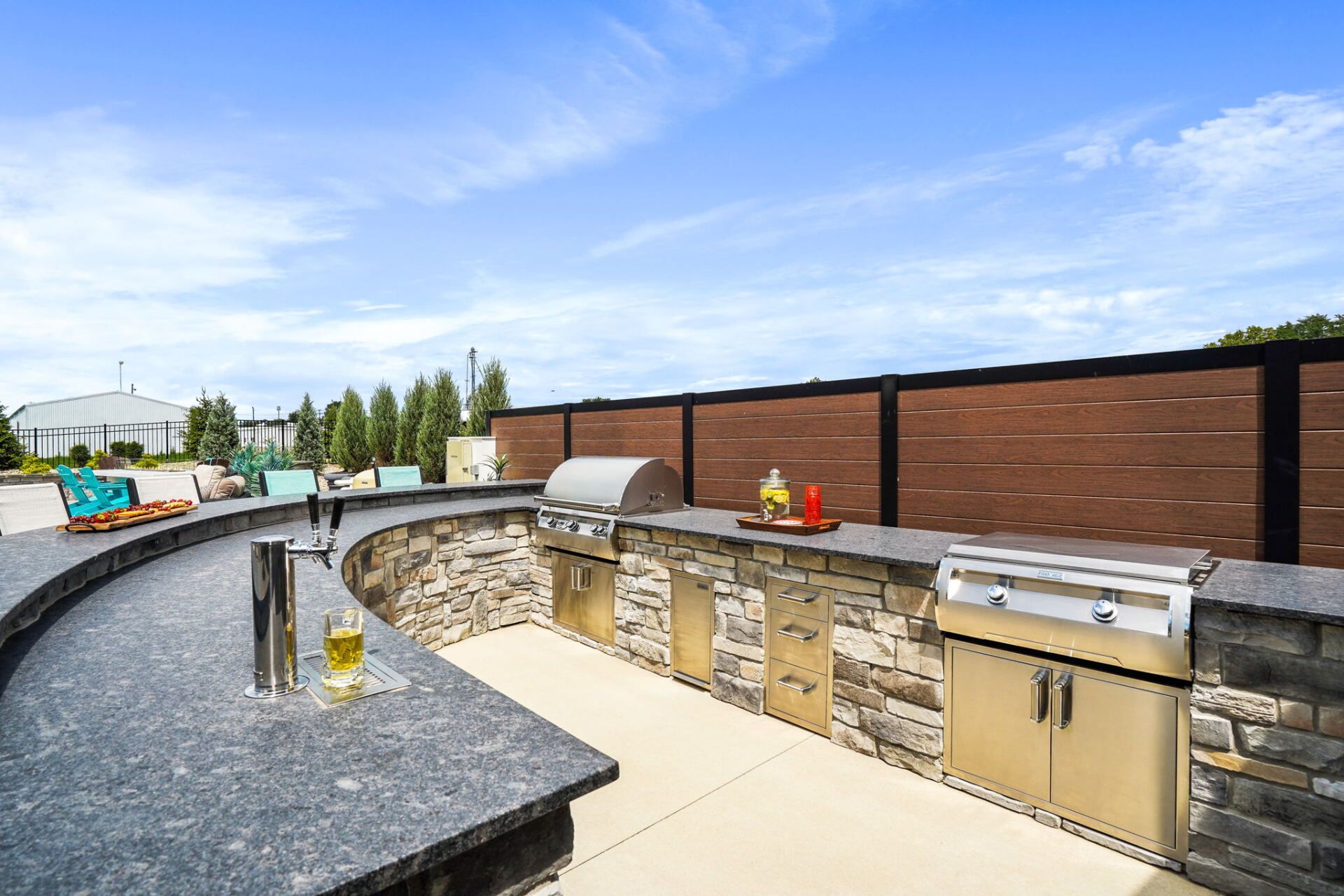 Outdoor kitchen with curved stone counters, built-in grill, and sink under a blue sky