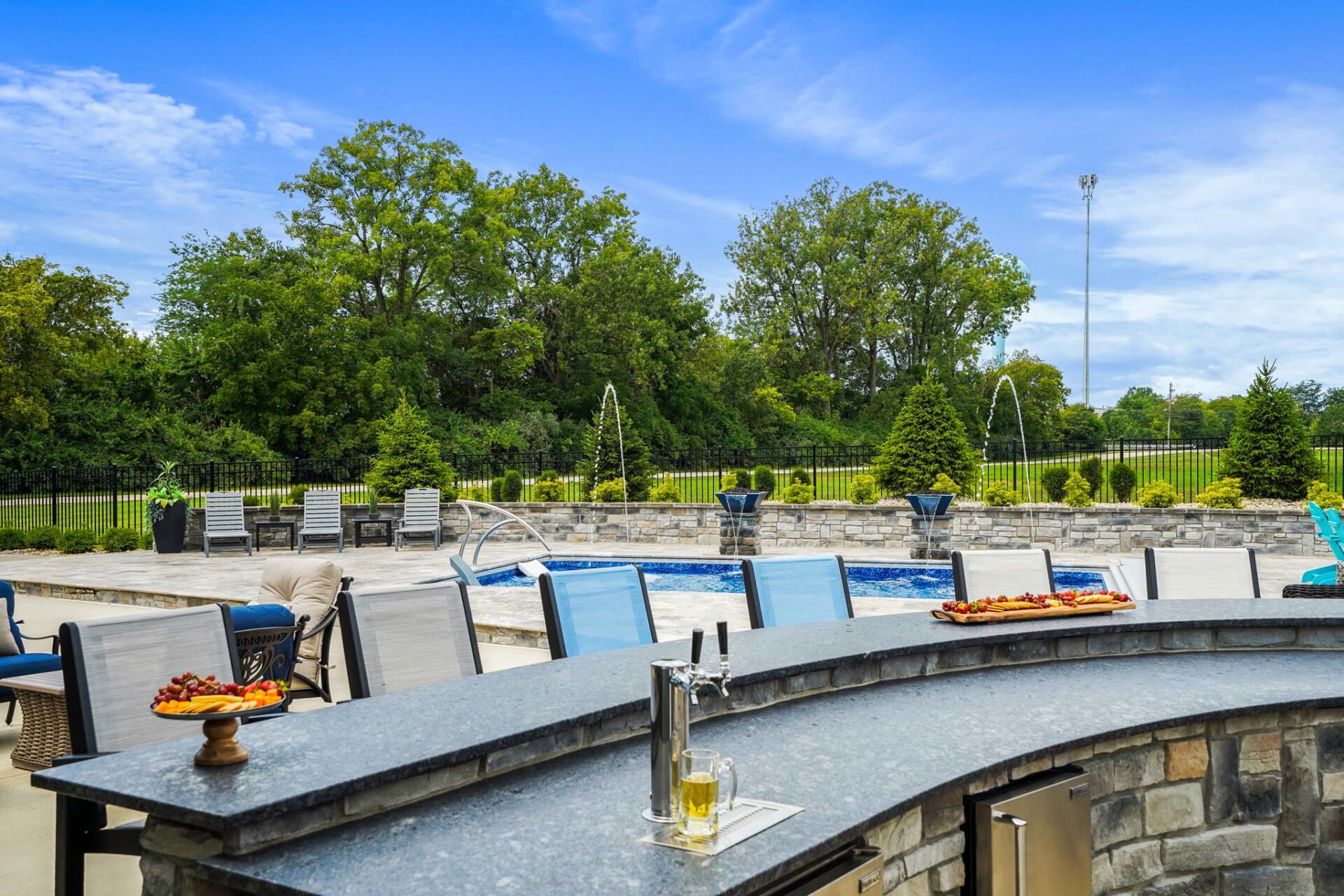 Outdoor patio with tables and chairs, stone railing, and trees under a blue sky