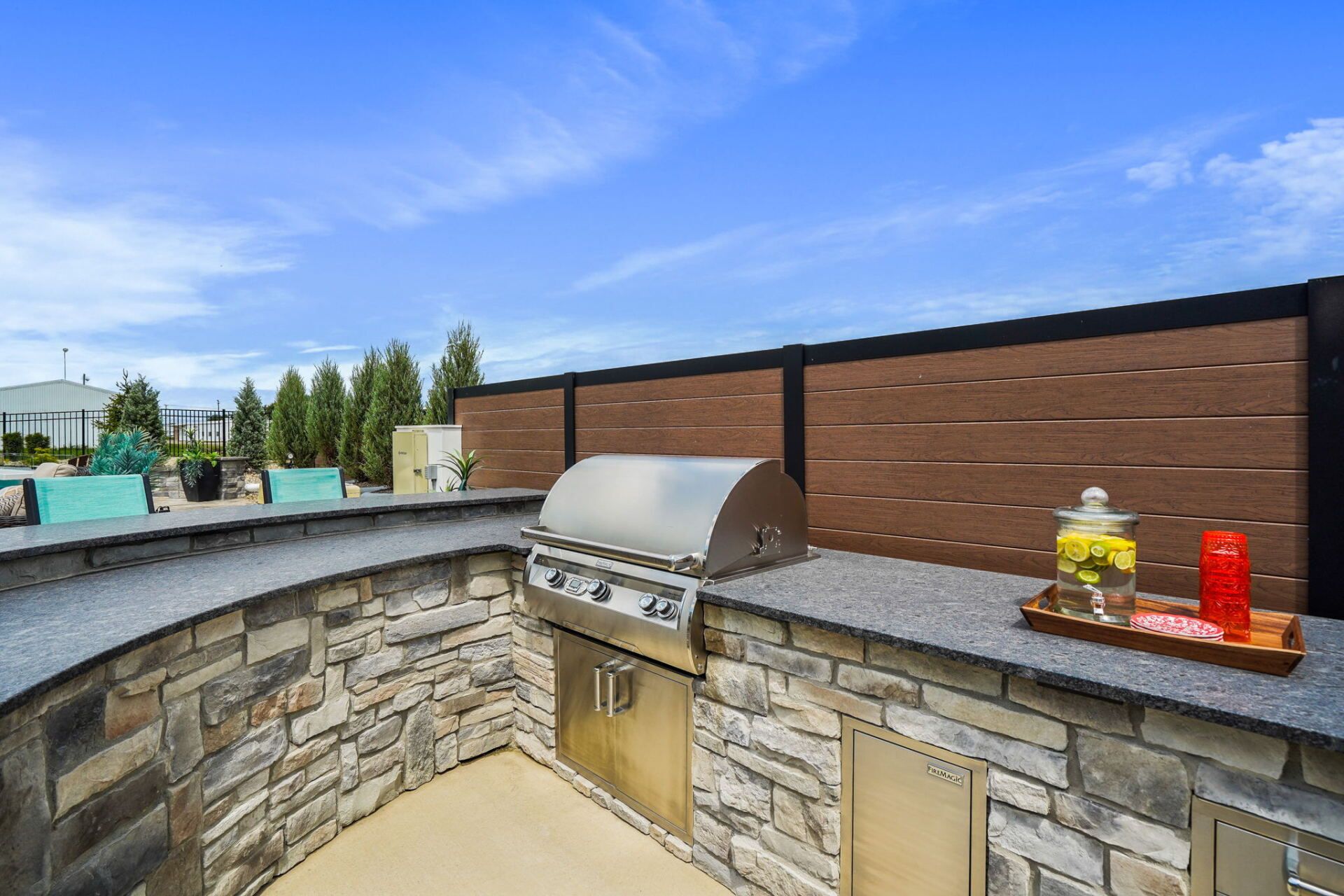 Outdoor stone patio with built-in grill, wooden privacy wall, and clear blue sky