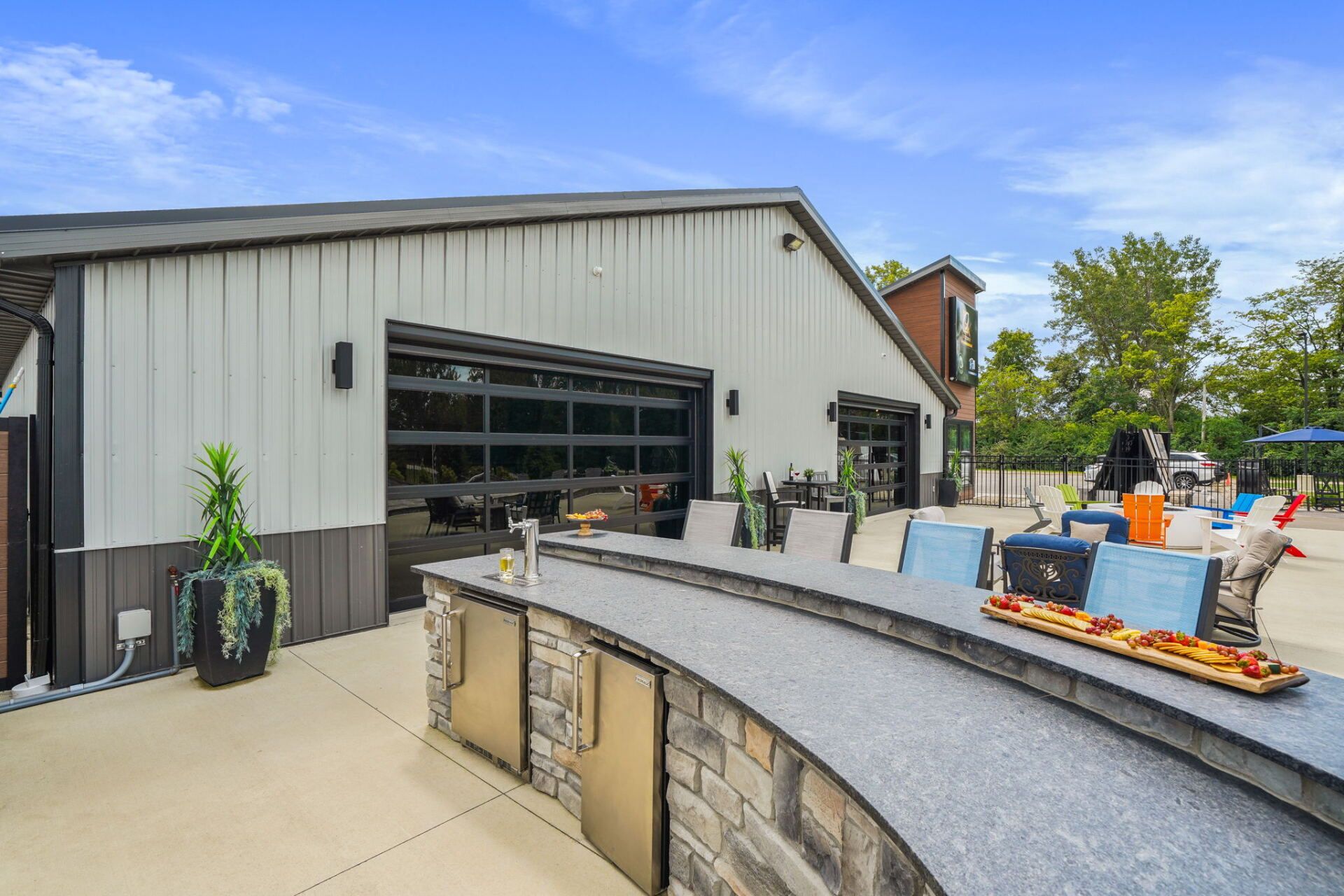 Outdoor patio beside a modern building with curved stone bar, lounge chairs, and a fire pit under blue sky