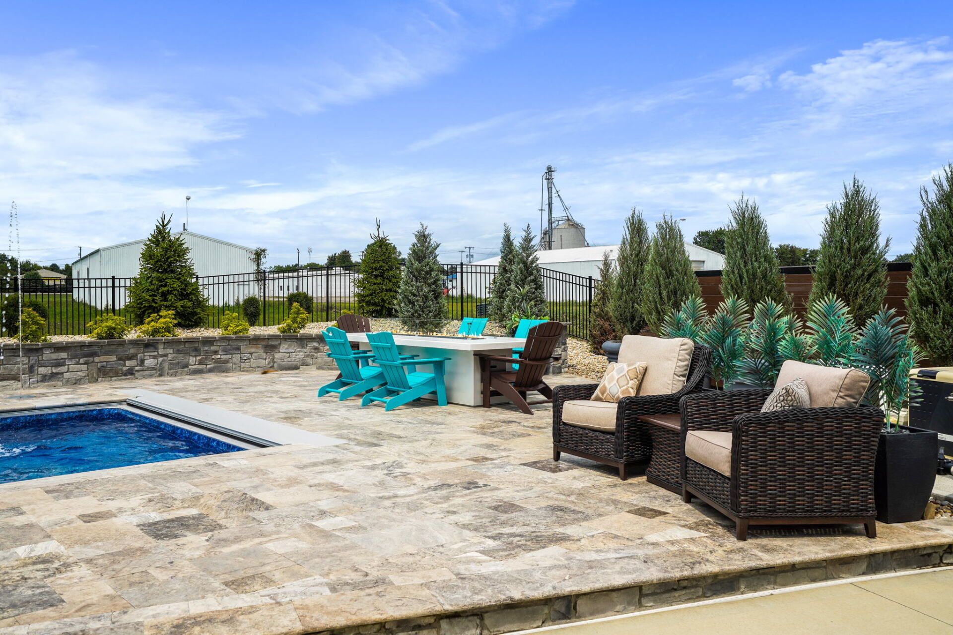 Backyard patio with pool, turquoise chairs, wicker seating, and potted plants under a blue sky