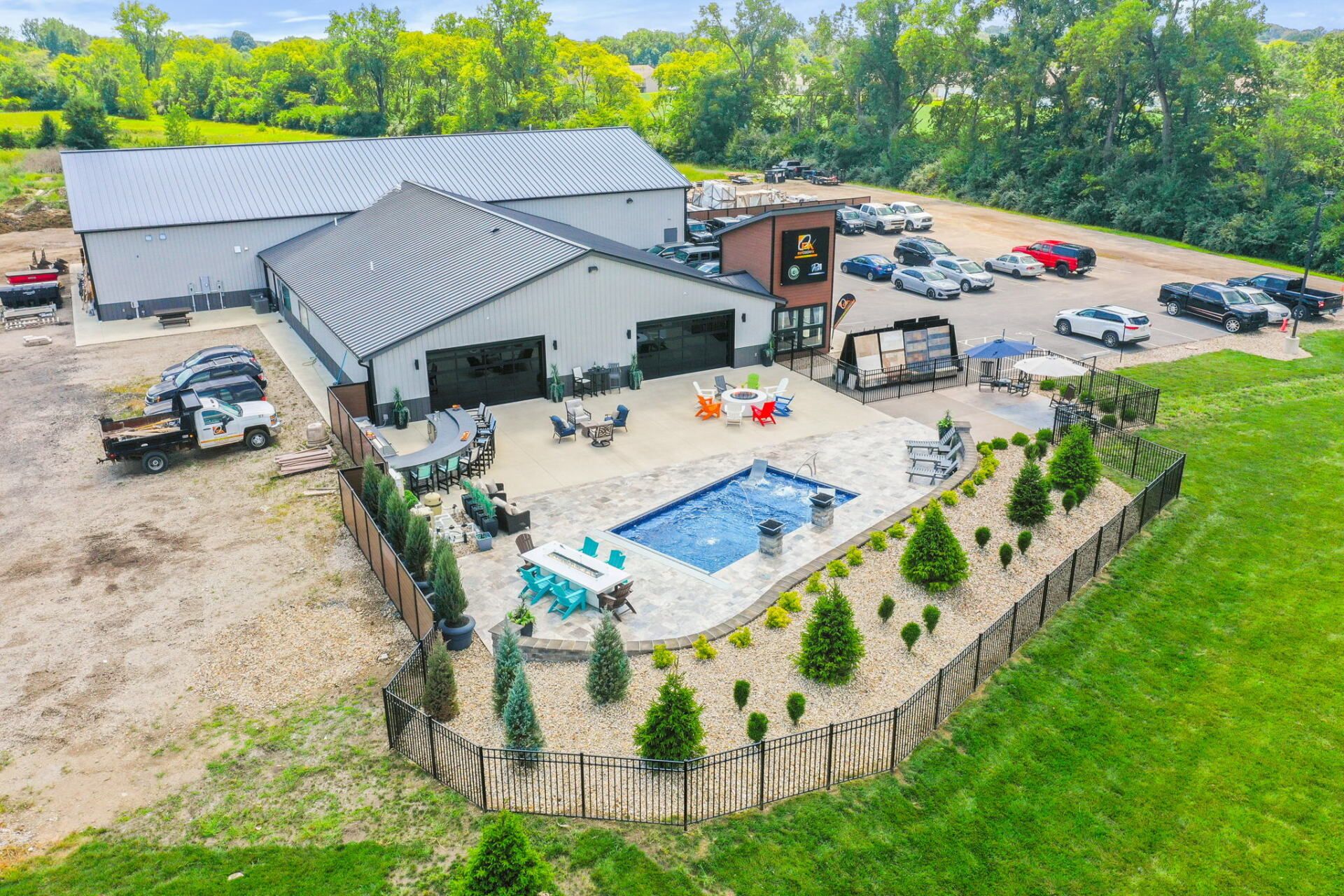 Aerial view of a house with a fenced backyard patio, pool, and parking lot surrounded by trees.