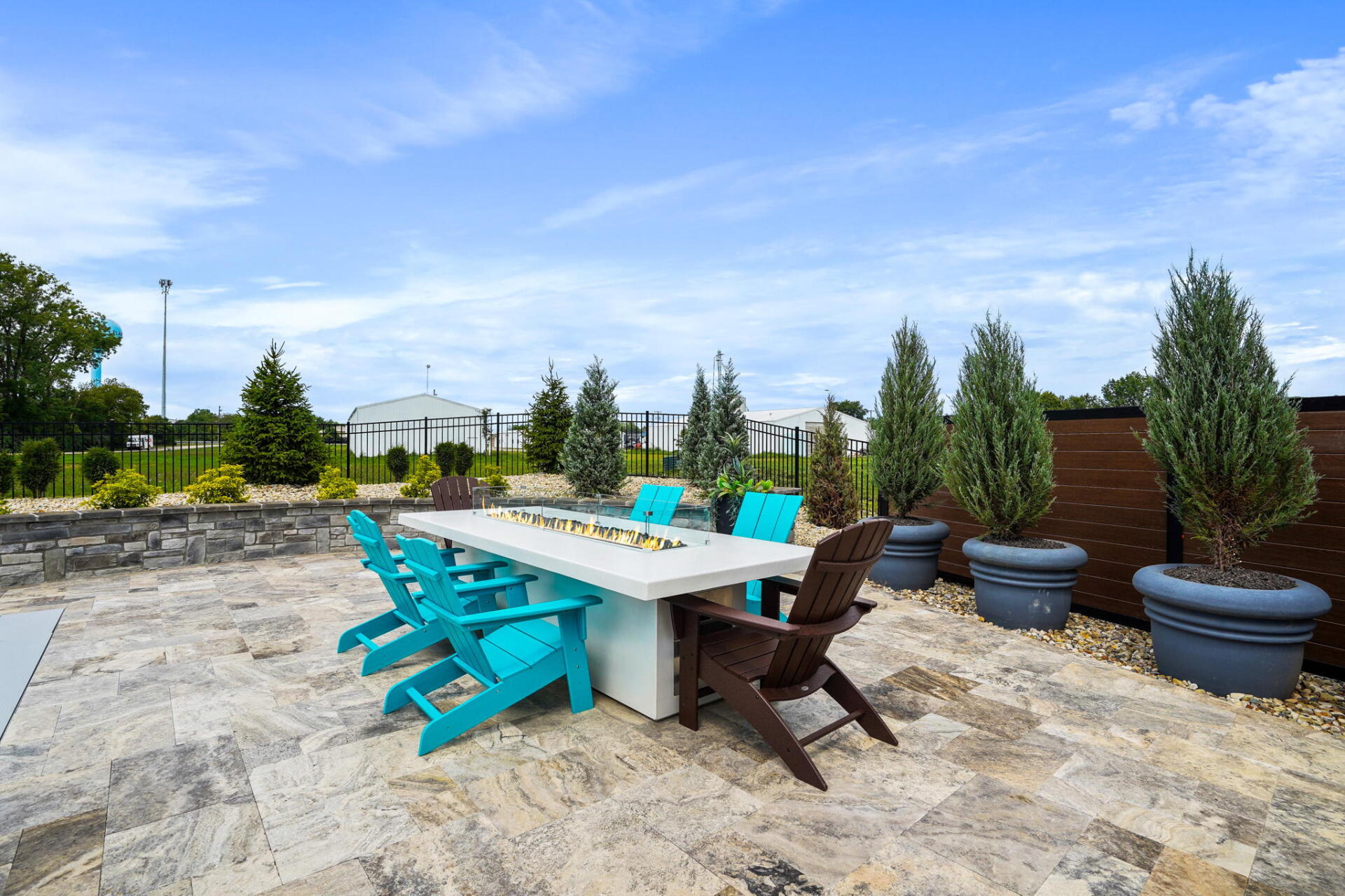 Patio dining area with turquoise and brown chairs, stone table, and potted trees under a blue sky