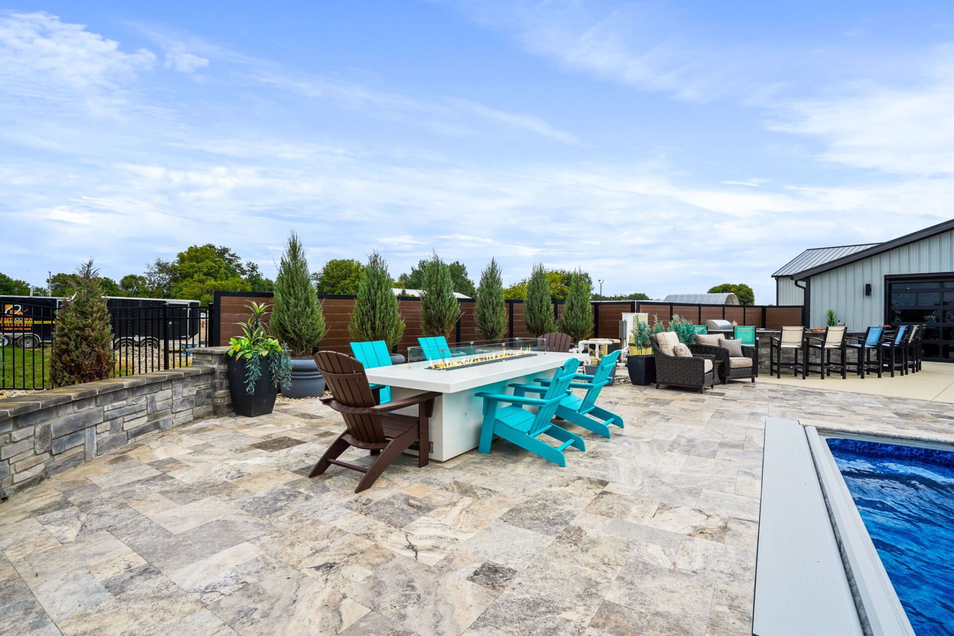 Outdoor patio with turquoise chairs and tables beside a swimming pool under a cloudy sky