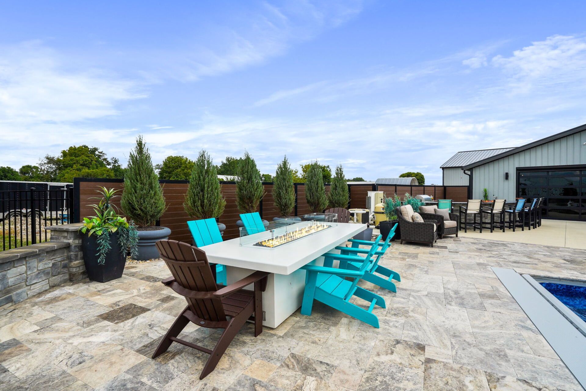 Outdoor patio with a long white table, turquoise chairs, and a stone walkway under a blue sky.