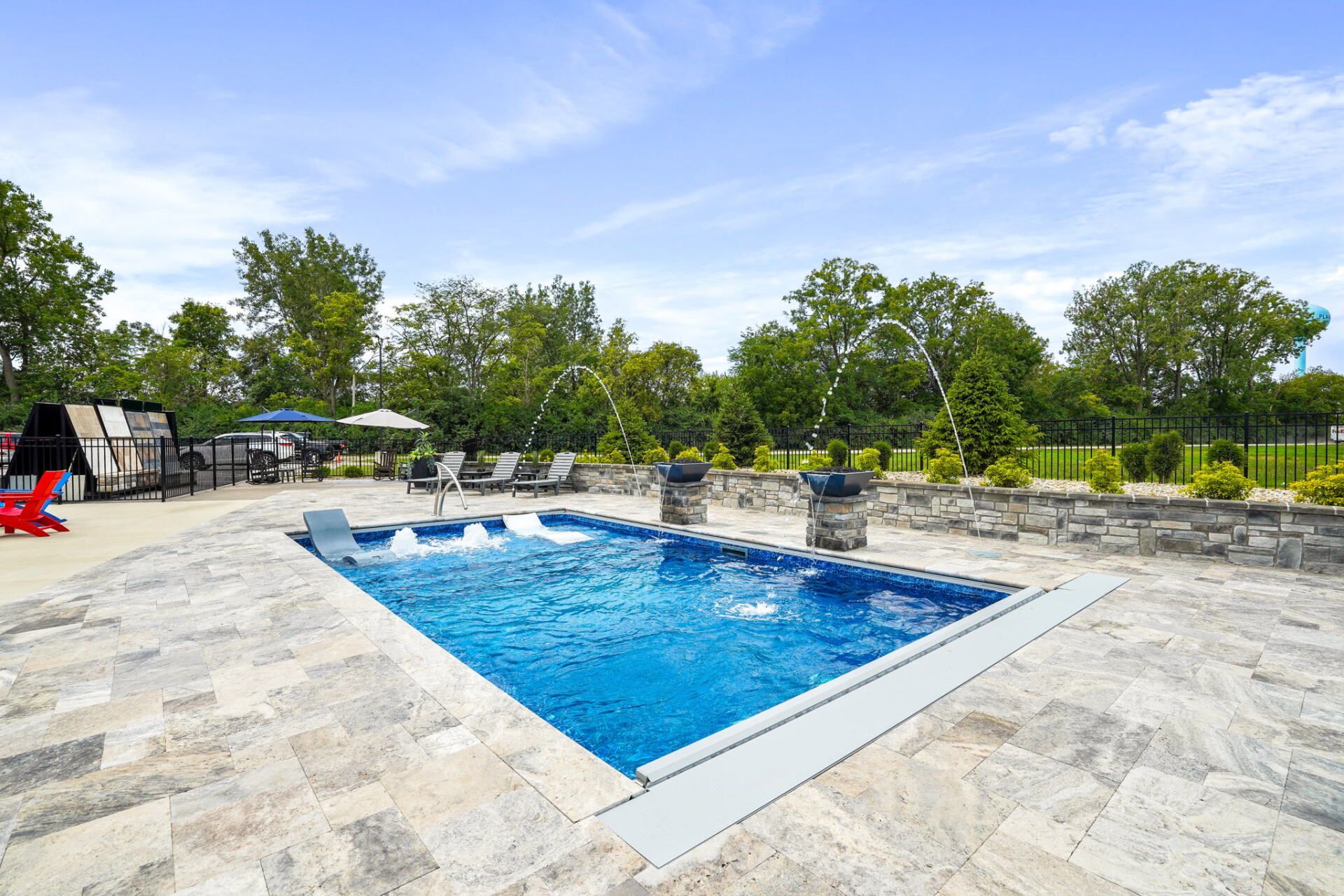 Outdoor swimming pool with blue water, stone deck, and trees under a sunny sky