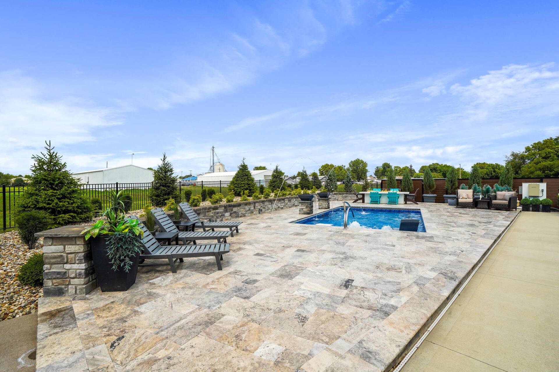 Poolside patio with lounge chairs, hot tub, and stone paving under a blue sky