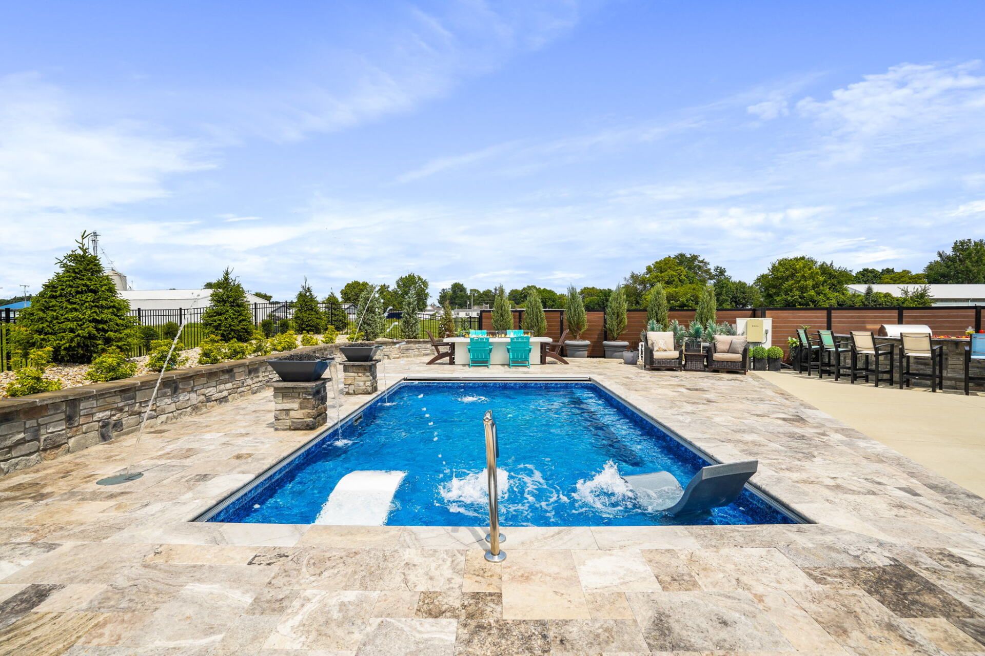 Outdoor pool with blue water and stone deck, surrounded by lounge chairs and trees under a bright sky