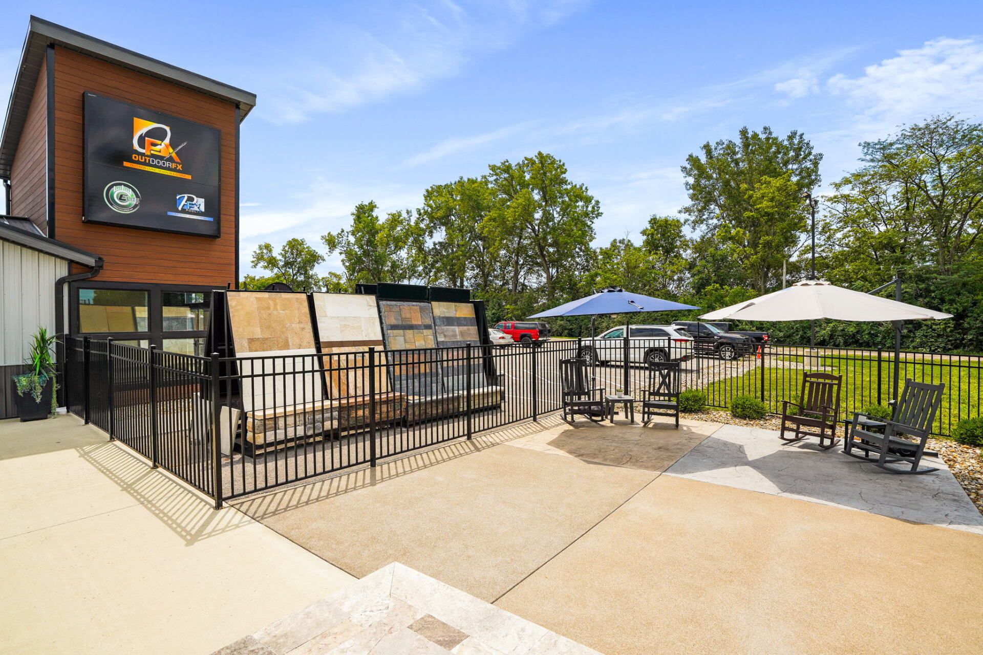 Outdoor patio seating beside a building, with umbrellas, chairs, and a fenced area in sunlight