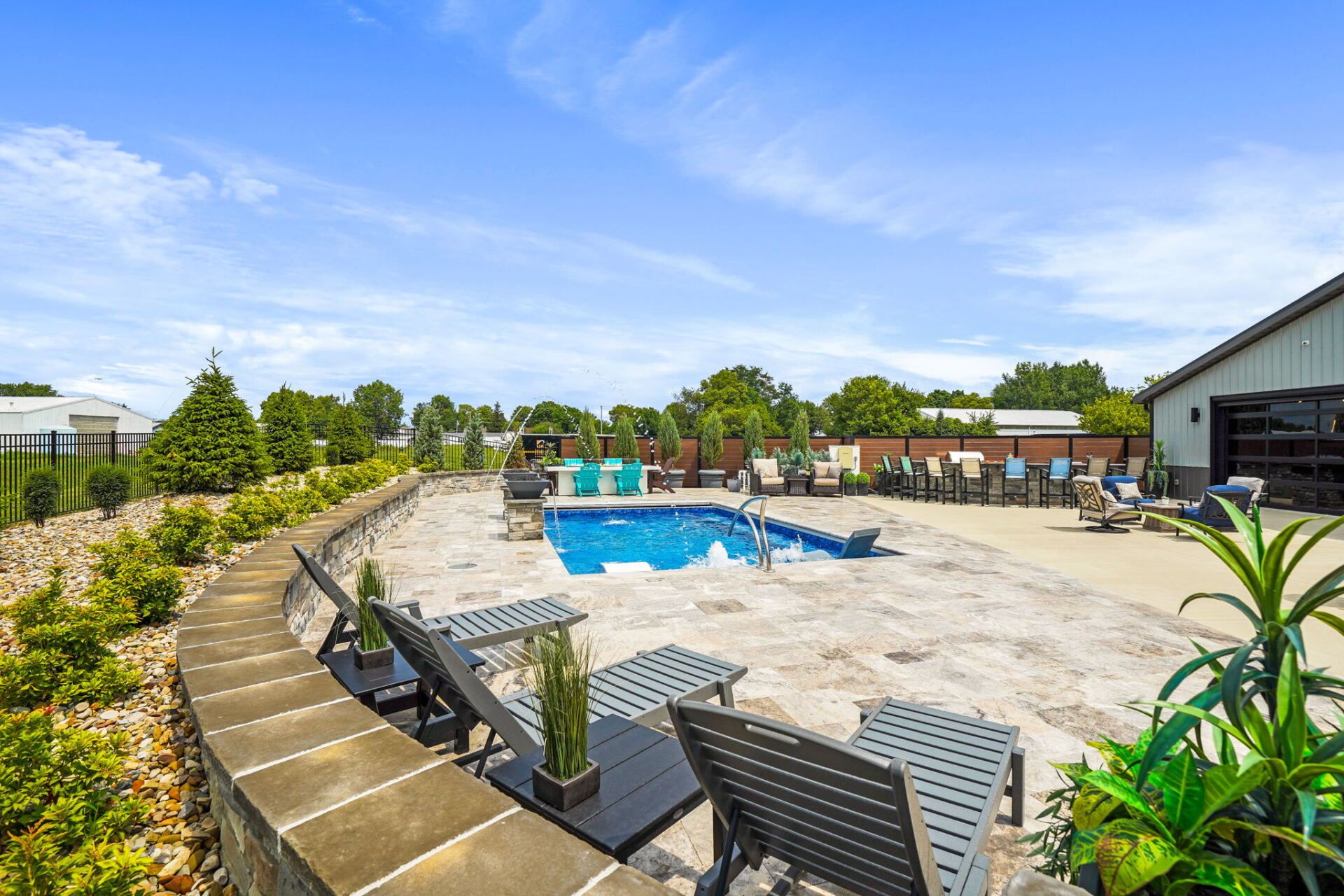 Outdoor resort pool with lounge chairs, stone deck, umbrellas, and blue water under a clear sky